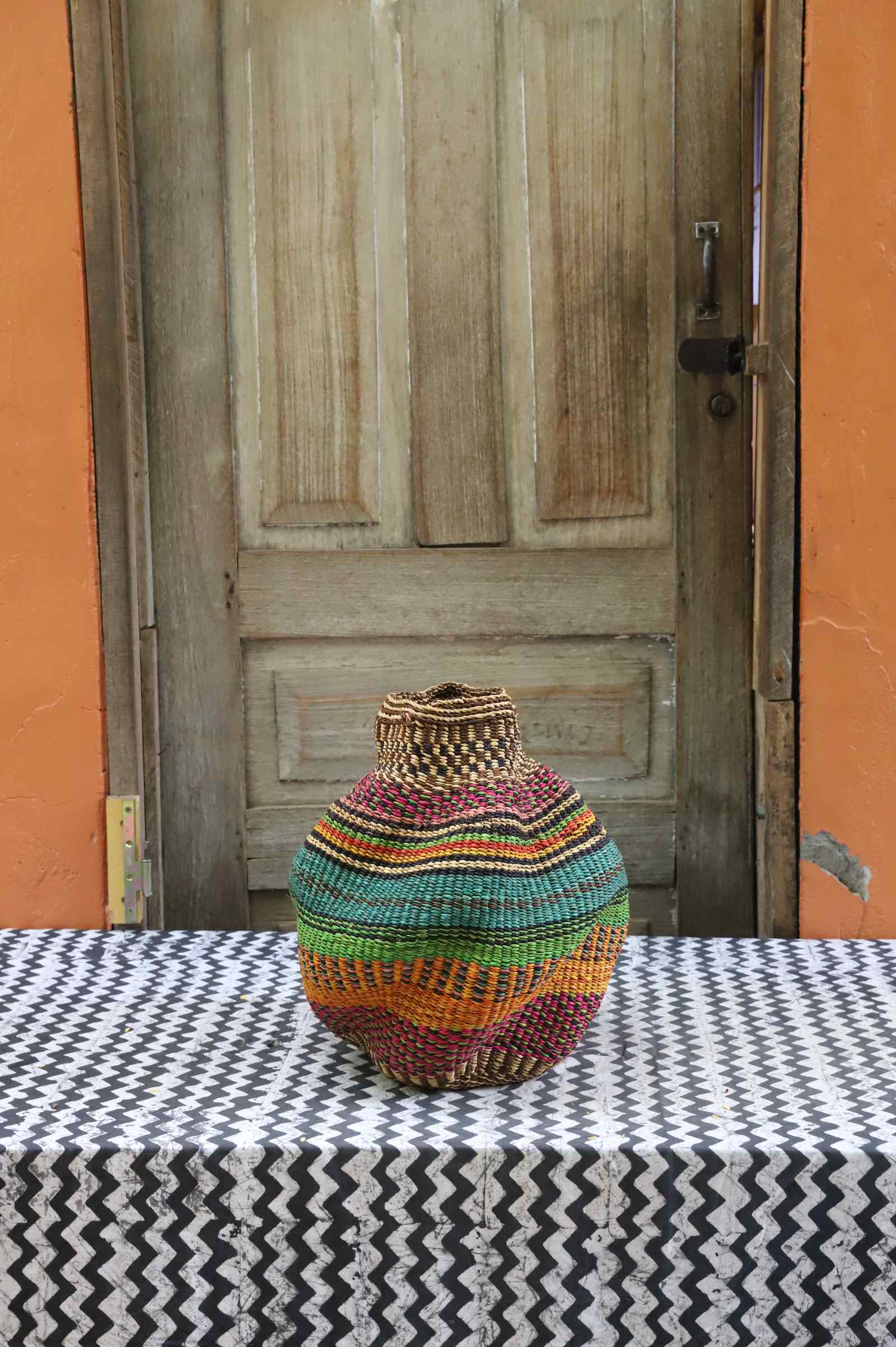 Handwoven Bolga art basket in a rounded pot shape, natural rim with a red, green and orange striped body.