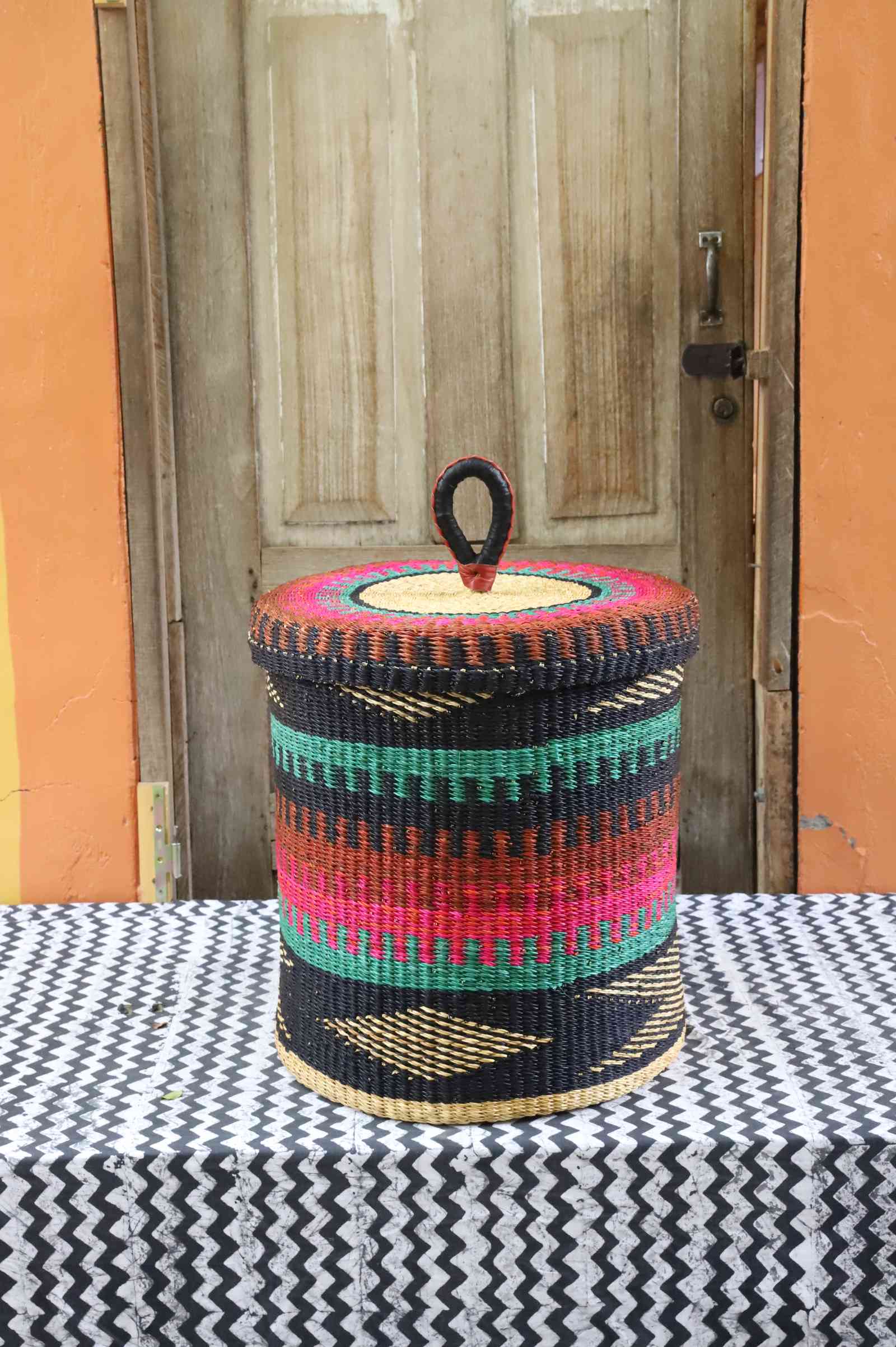 Lidded laundry basket in teal, pink and rust banded weave with a black zigzag base, styled on a chevron cloth.