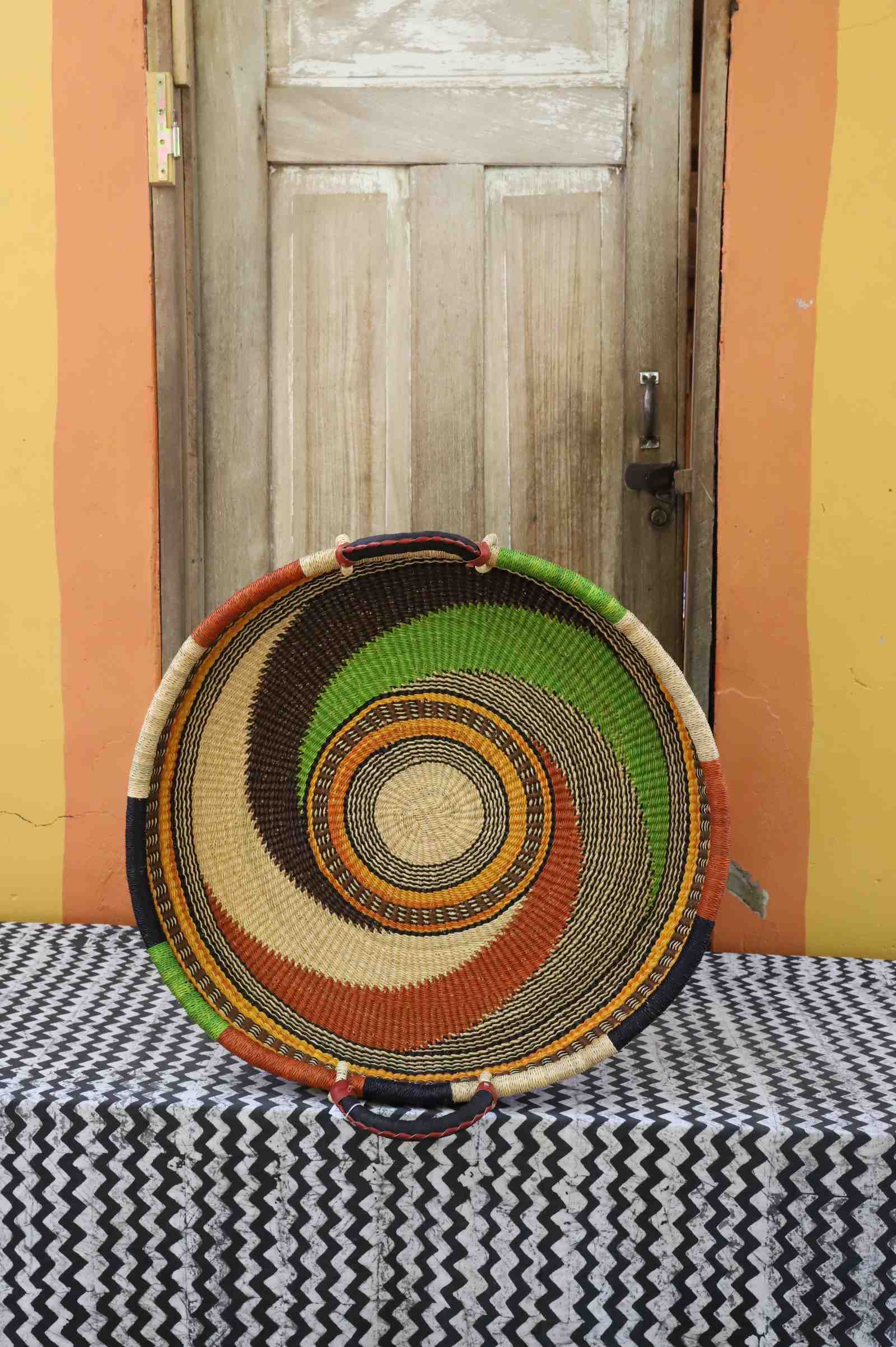 Medium handwoven Bolga wall tray disc with green, orange and black swirl and natural centre.