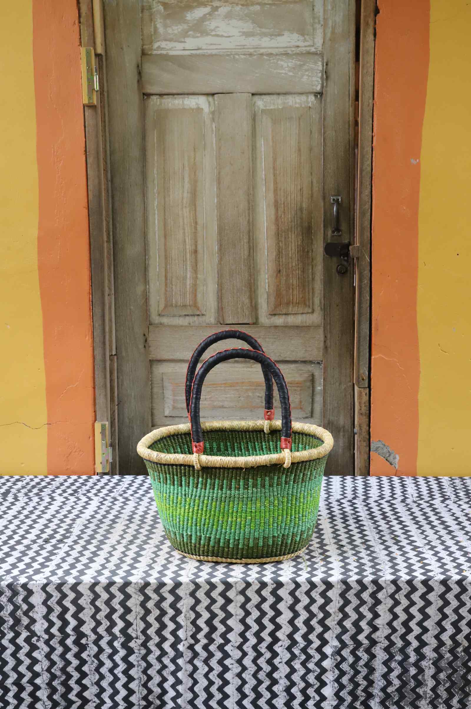 Small handwoven oval Bolga shopping basket in natural straw with green banded stripes and dark handles.