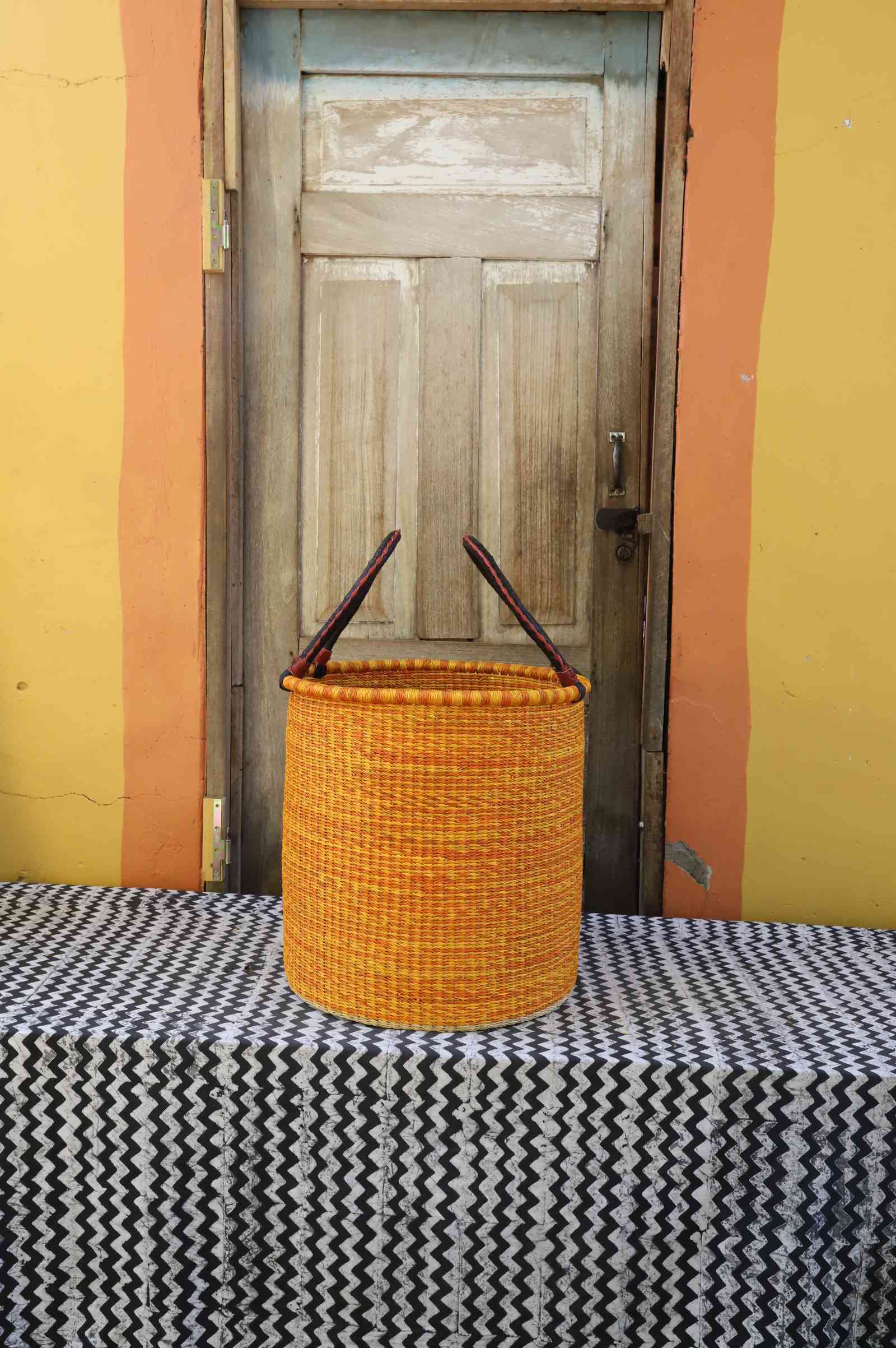 Medium handwoven open-top Bolga laundry basket dyed bold orange with a plain woven body.