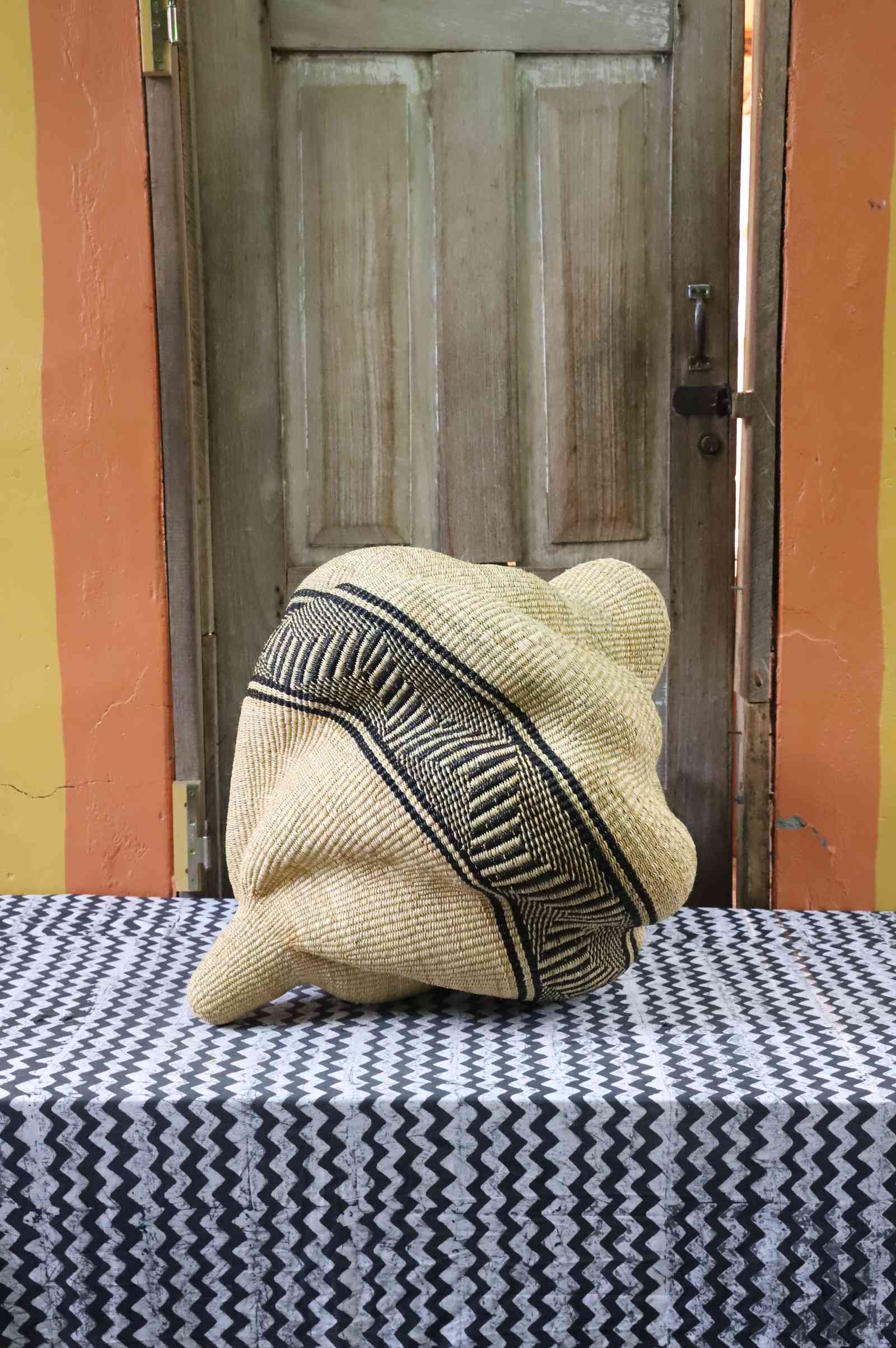 Natural straw Bolga basket in a coiled spiral shape with a black geometric band, shown from a rear angle on a tablecloth.