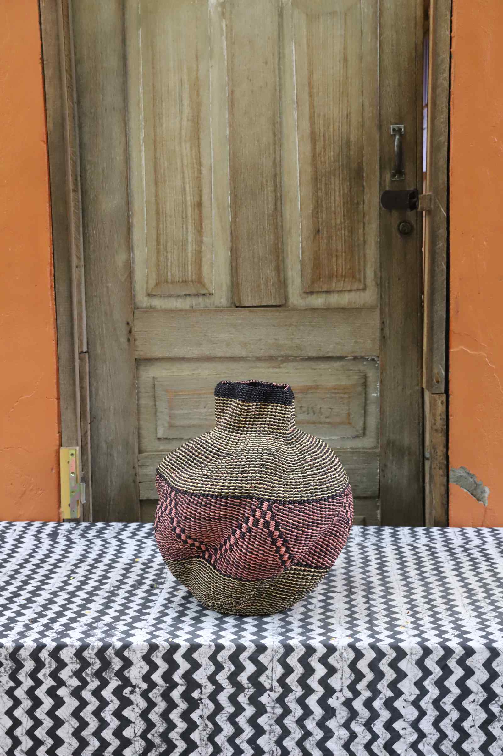 Handwoven Bolga art basket in a rounded pot shape, natural straw with a dark diamond weave and red centre.
