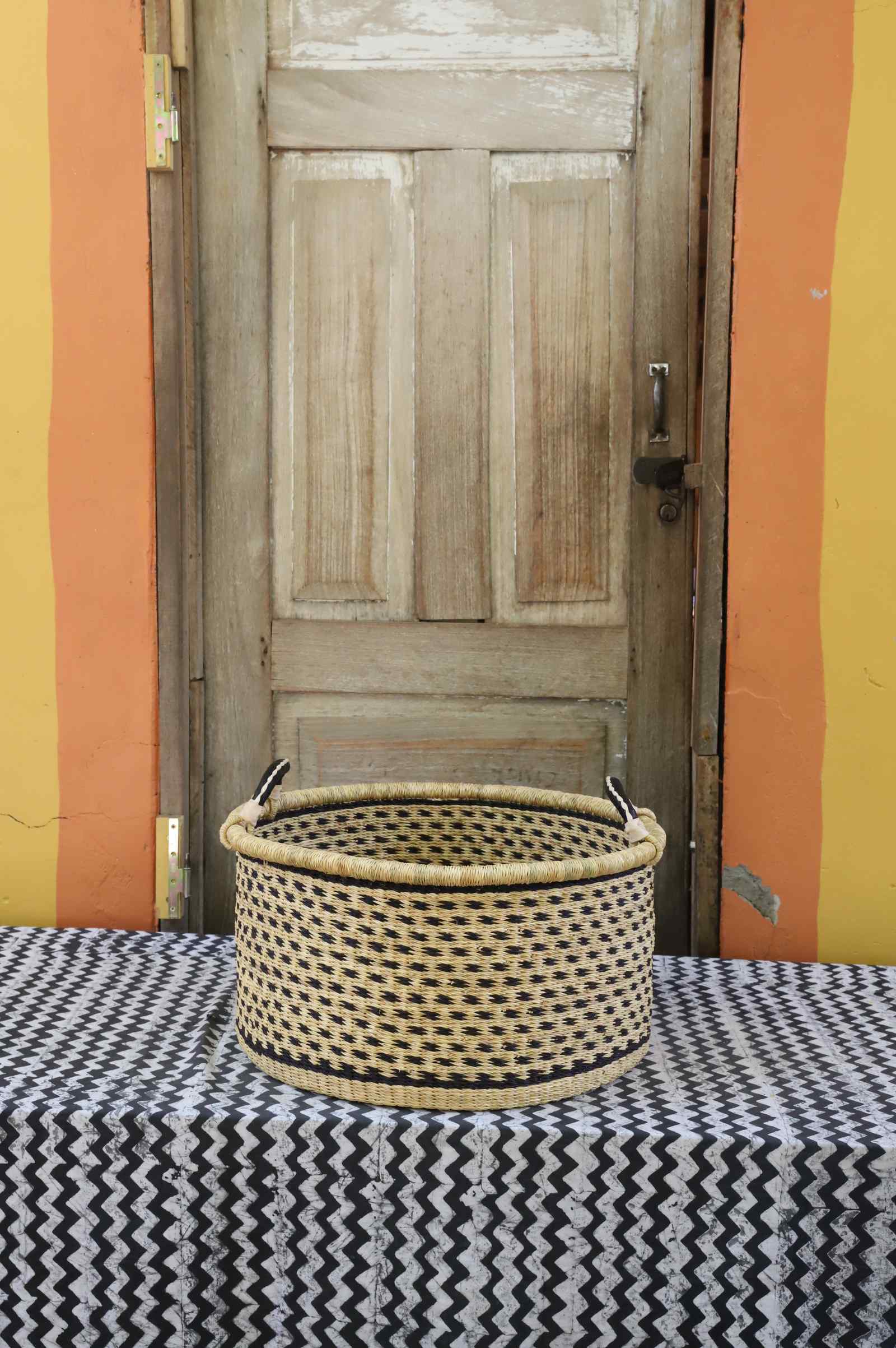 Medium handwoven Bolga storage tub in plain natural straw with a fine diagonal weave and dark handles.