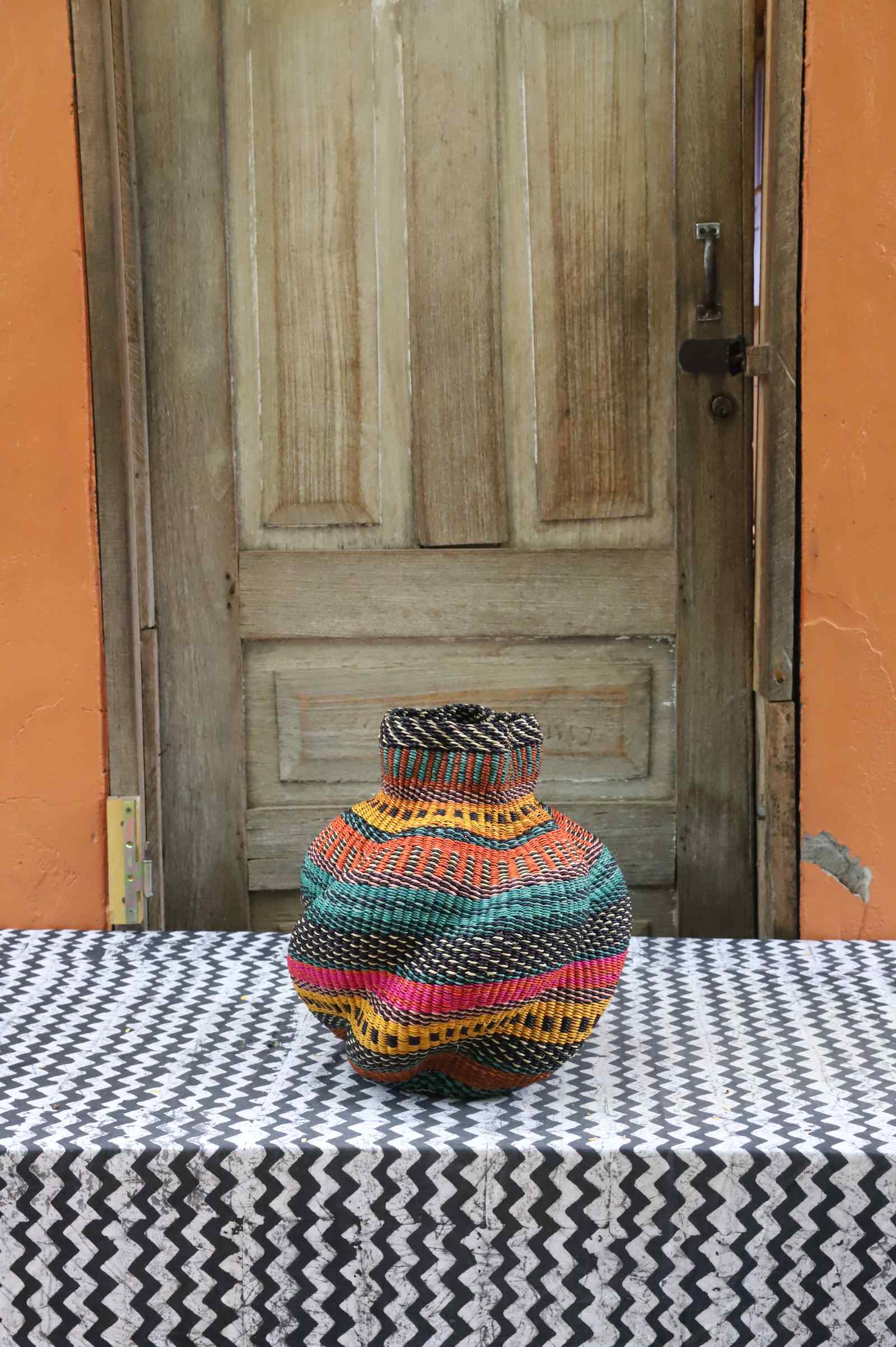 Handwoven Bolga art basket in a rounded pot shape, fine multicolour striped body with a natural rim.