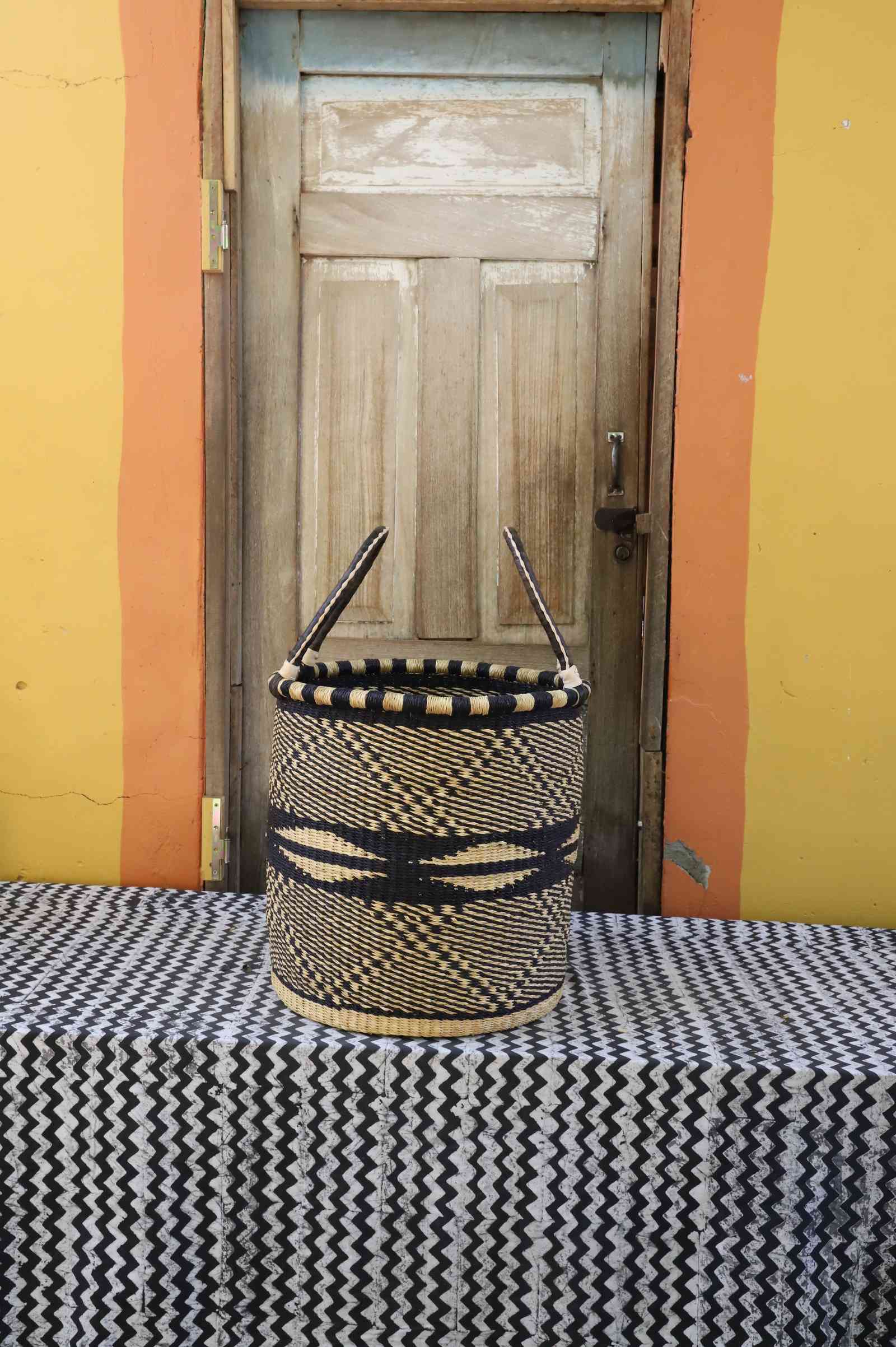 Medium handwoven open-top Bolga laundry basket in natural straw with black wave and wing motifs.