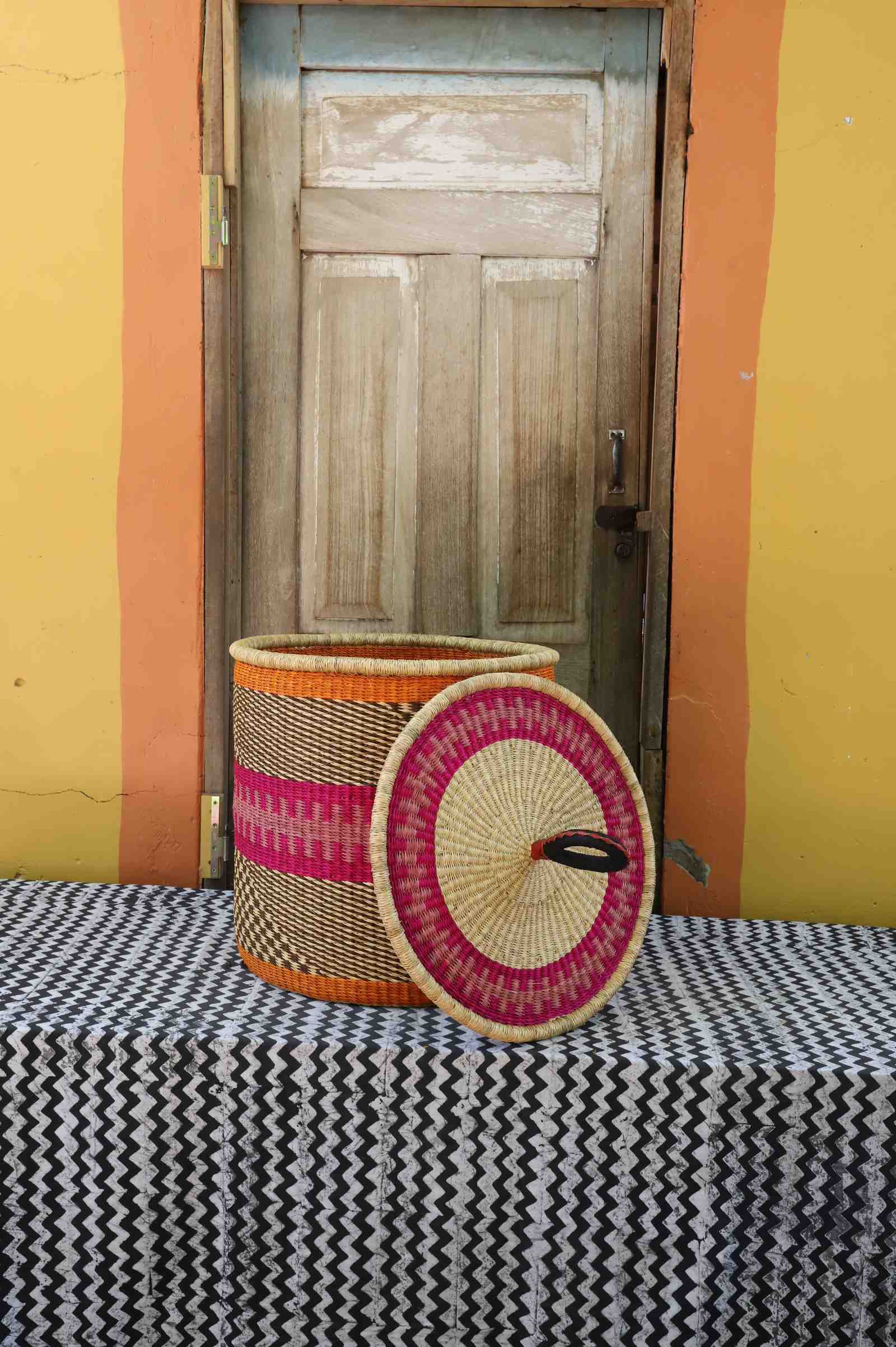 Handwoven Bolga laundry basket with lid removed, natural body with pink-and-orange band and multicolour lid.