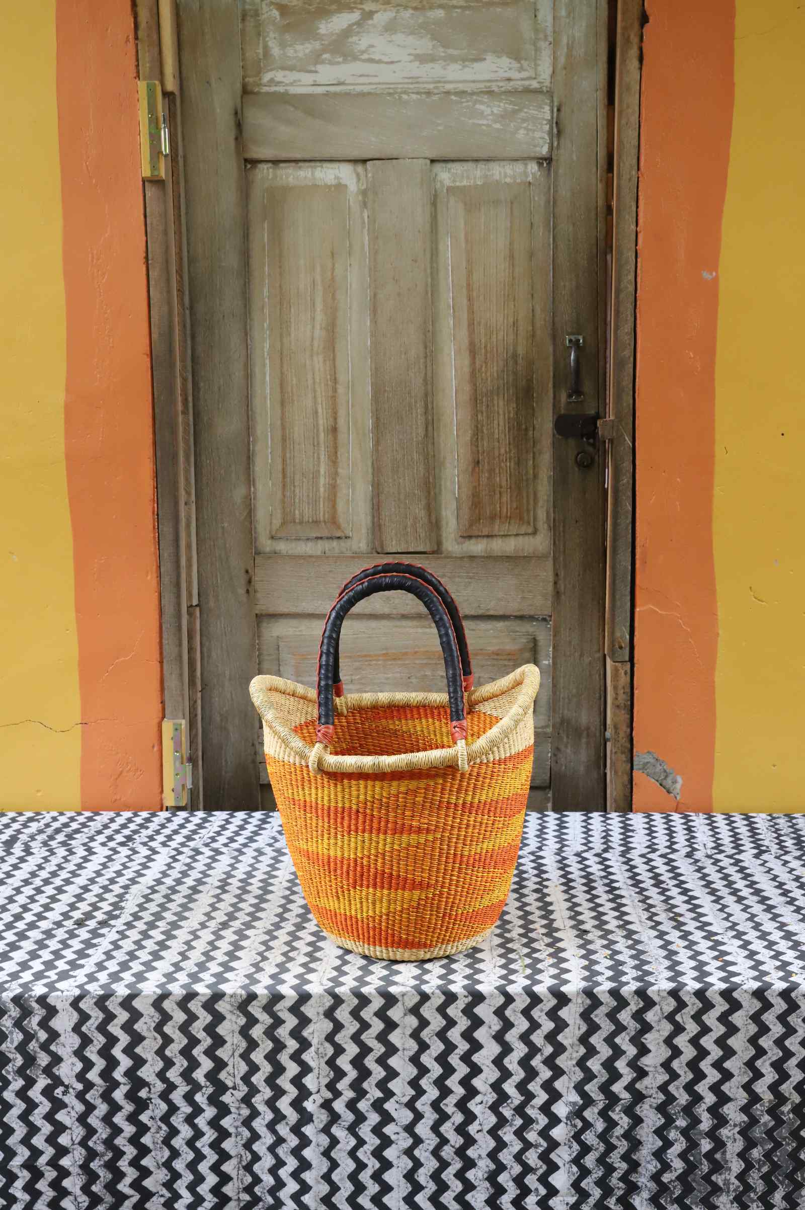 Medium handwoven Nyariga Bolga shopping basket in dyed bold orange with a plain woven body and dark handles.