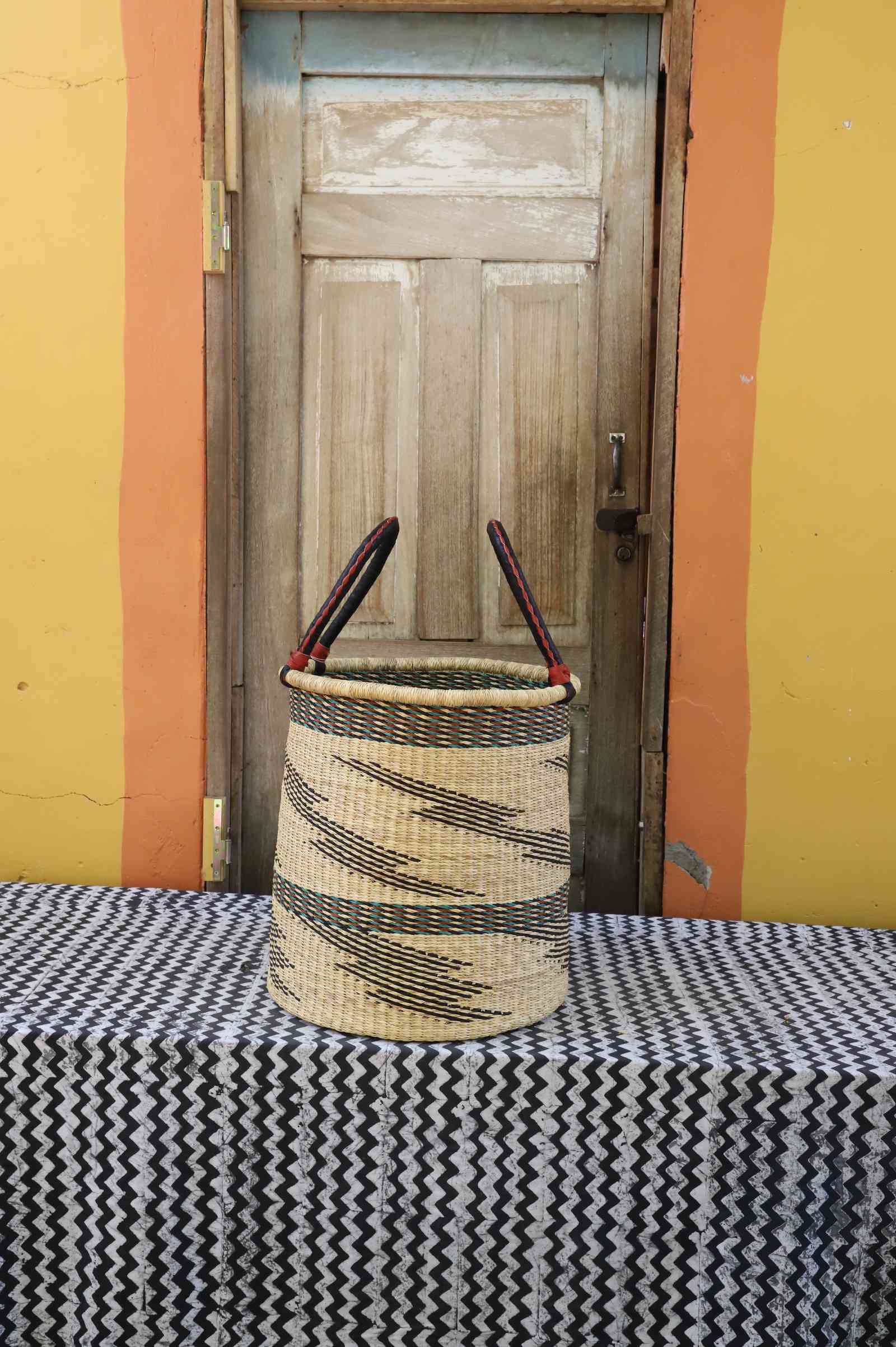 Medium handwoven open-top Bolga laundry basket in natural straw with scattered black wave motifs.