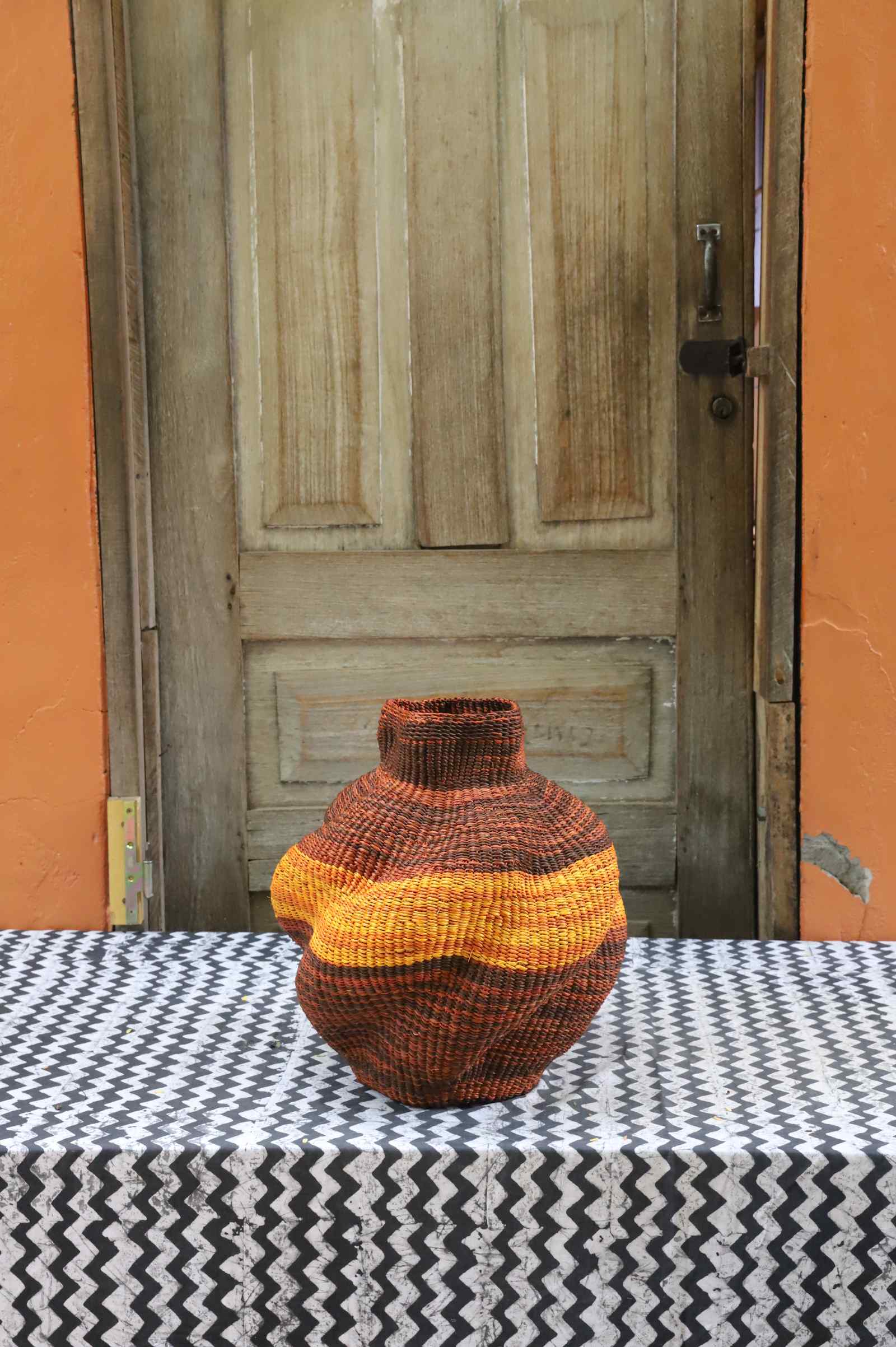 Handwoven Bolga art basket in a rounded pot shape, dyed rust-red with a yellow and orange central band.
