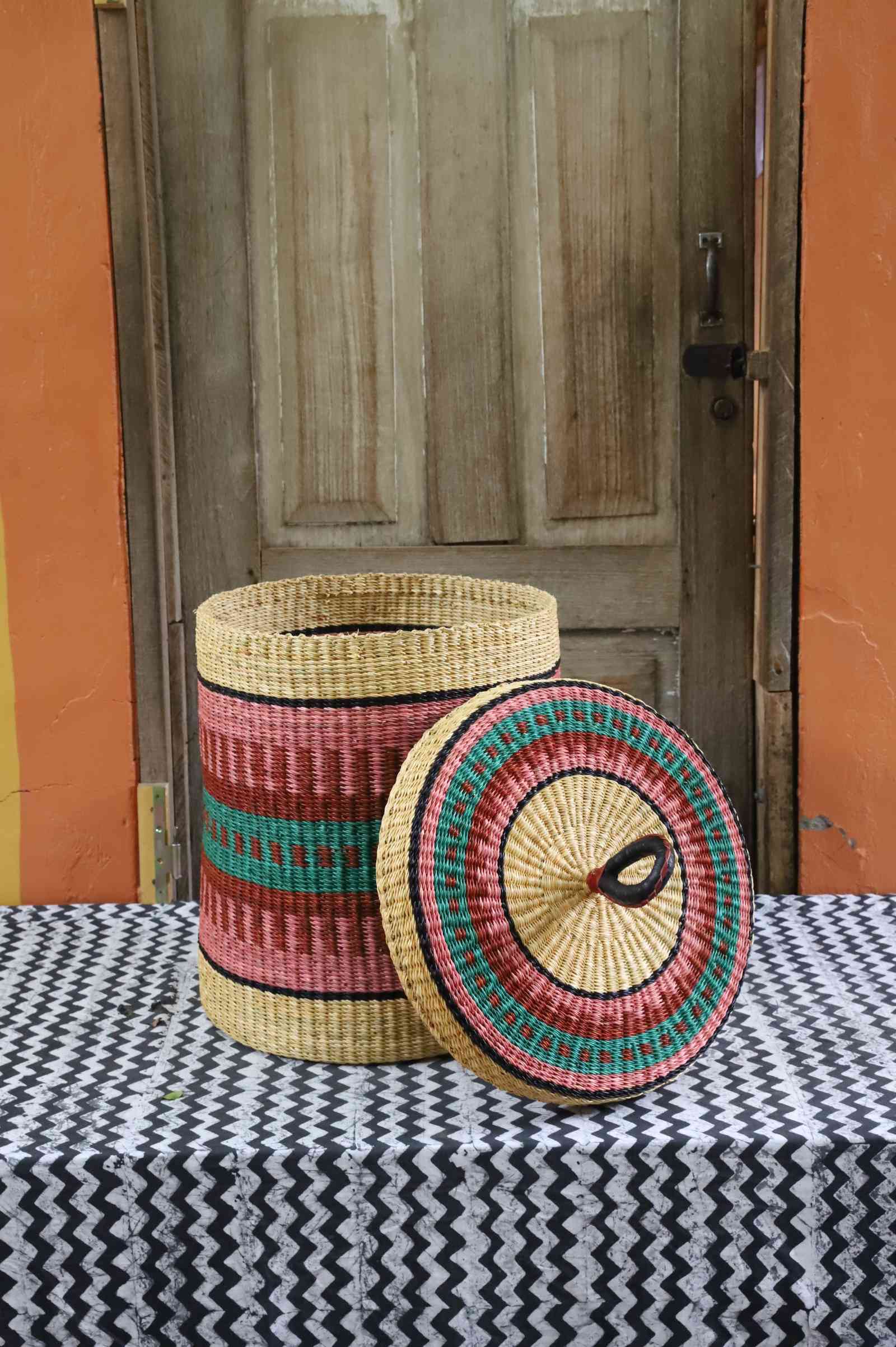 Lidded laundry basket in natural straw with pink and teal striped banding, lid resting alongside on a chevron cloth.