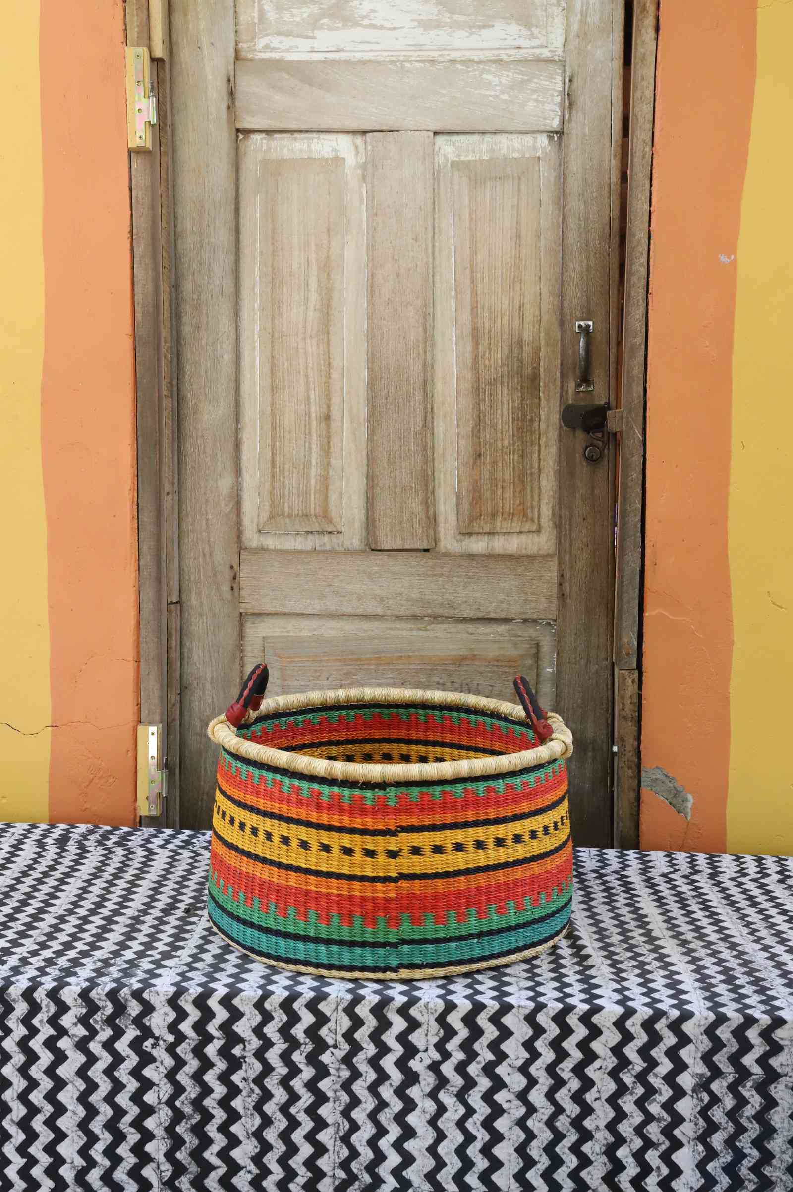 Medium handwoven Bolga storage tub in dyed green with orange and yellow banded stripes and dark handles.
