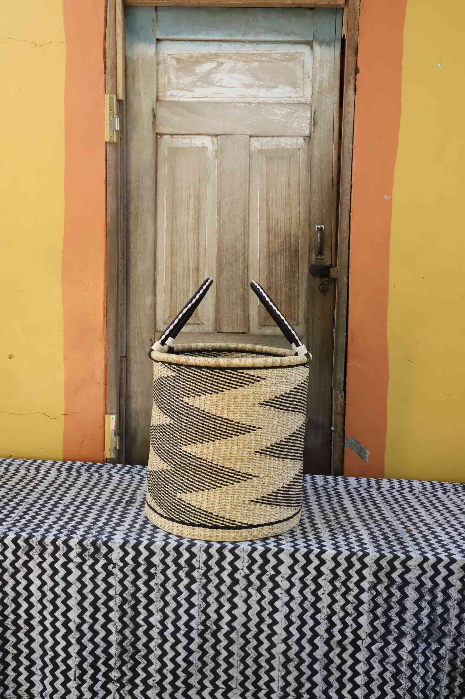 Medium handwoven open-top Bolga laundry basket in natural straw with black jagged sawtooth stripes.
