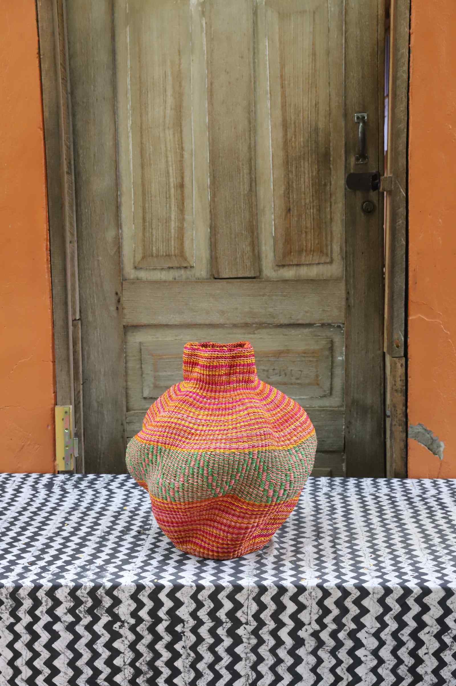 Handwoven Bolga art basket in a rounded pot shape, natural body with fine pink and orange banded stripes.