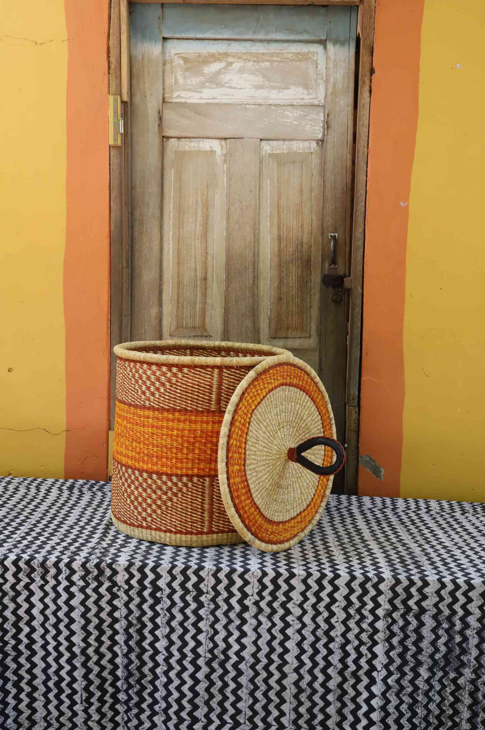 Handwoven Bolga laundry basket with lid removed, natural body with orange central band and coiled lid.