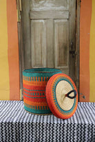 Handwoven Bolga laundry basket with lid removed, showing an orange and teal striped body and lid.