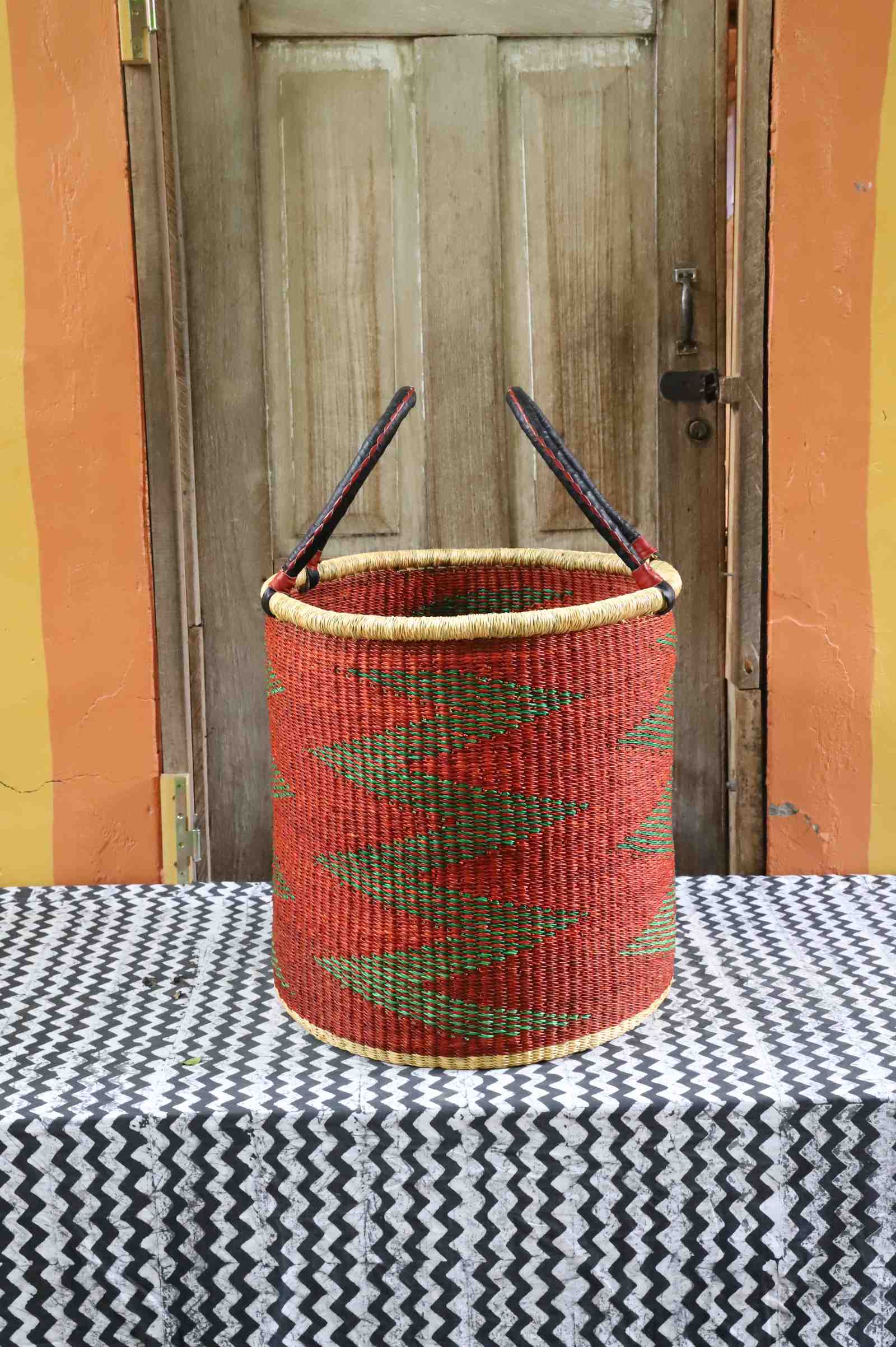 Large open laundry basket in red and green zigzag weave with arched handles, styled on a chevron cloth.