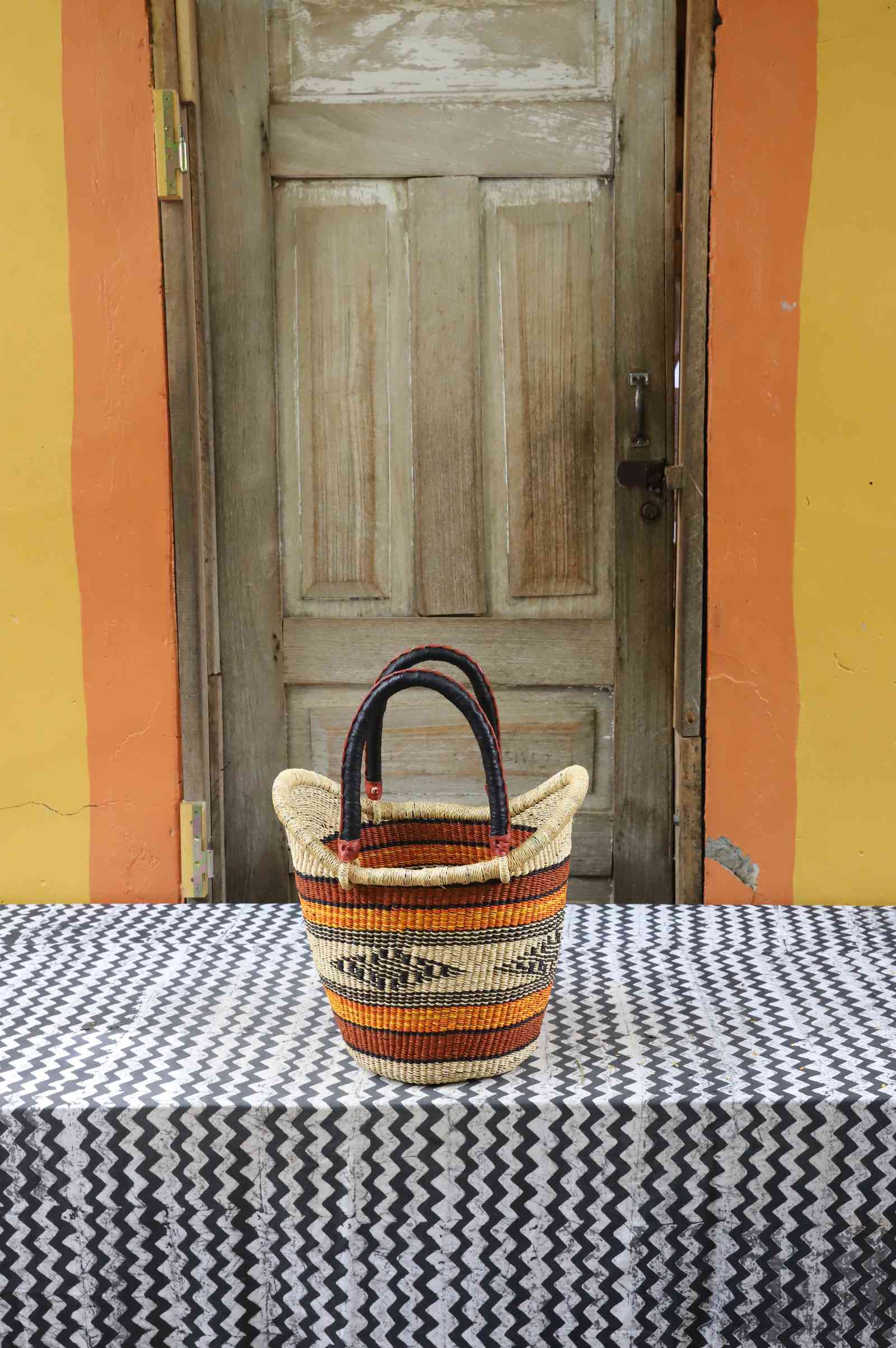 Small handwoven Nyariga Bolga shopping basket in orange and red fine banded stripes with dark handles.