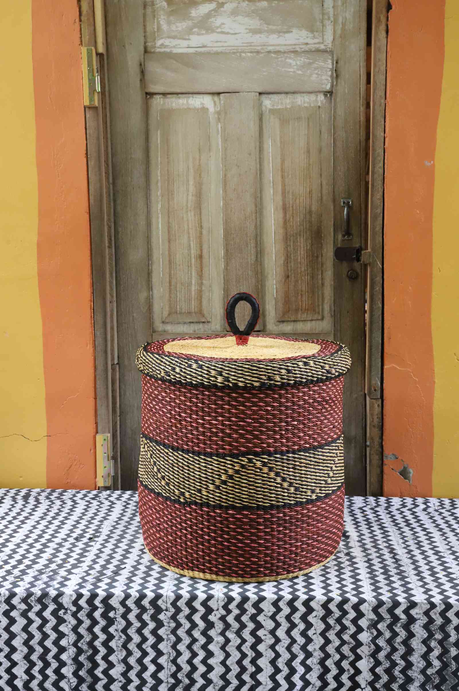 Handwoven Bolga laundry basket with lid in deep red with a black woven accent band and natural straw lid.