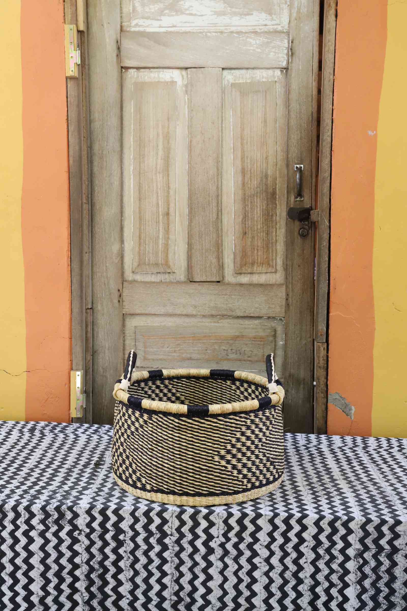 Small handwoven Bolga storage tub in natural straw with fine checker weave and dark leather-wrapped rim.