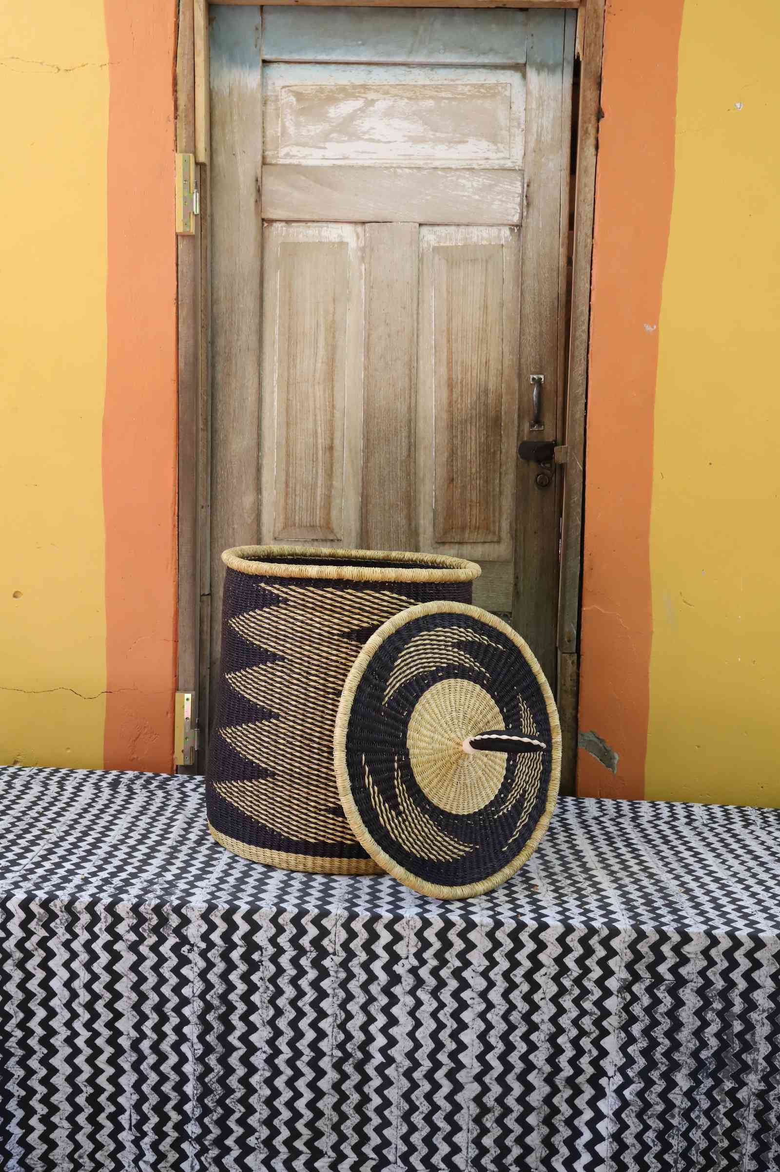 Handwoven Bolga laundry basket with lid removed, natural body with black zigzag and coiled rim lid.