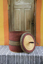 Handwoven Bolga laundry basket with lid removed, showing a deep red body with black accent and natural lid.