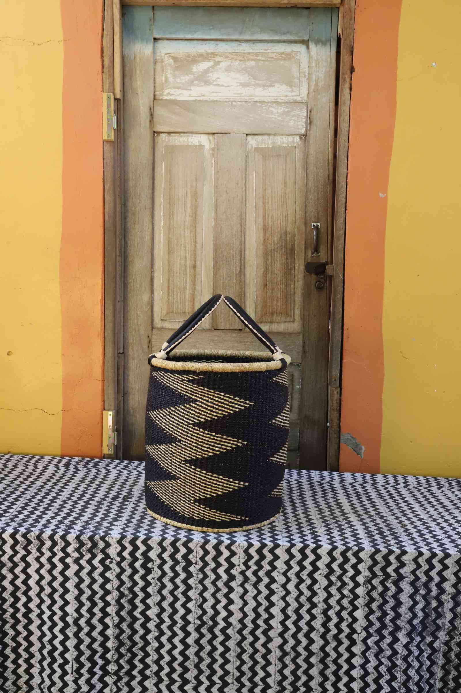 Small handwoven open-top Bolga laundry basket in natural straw with a bold black zigzag pattern.