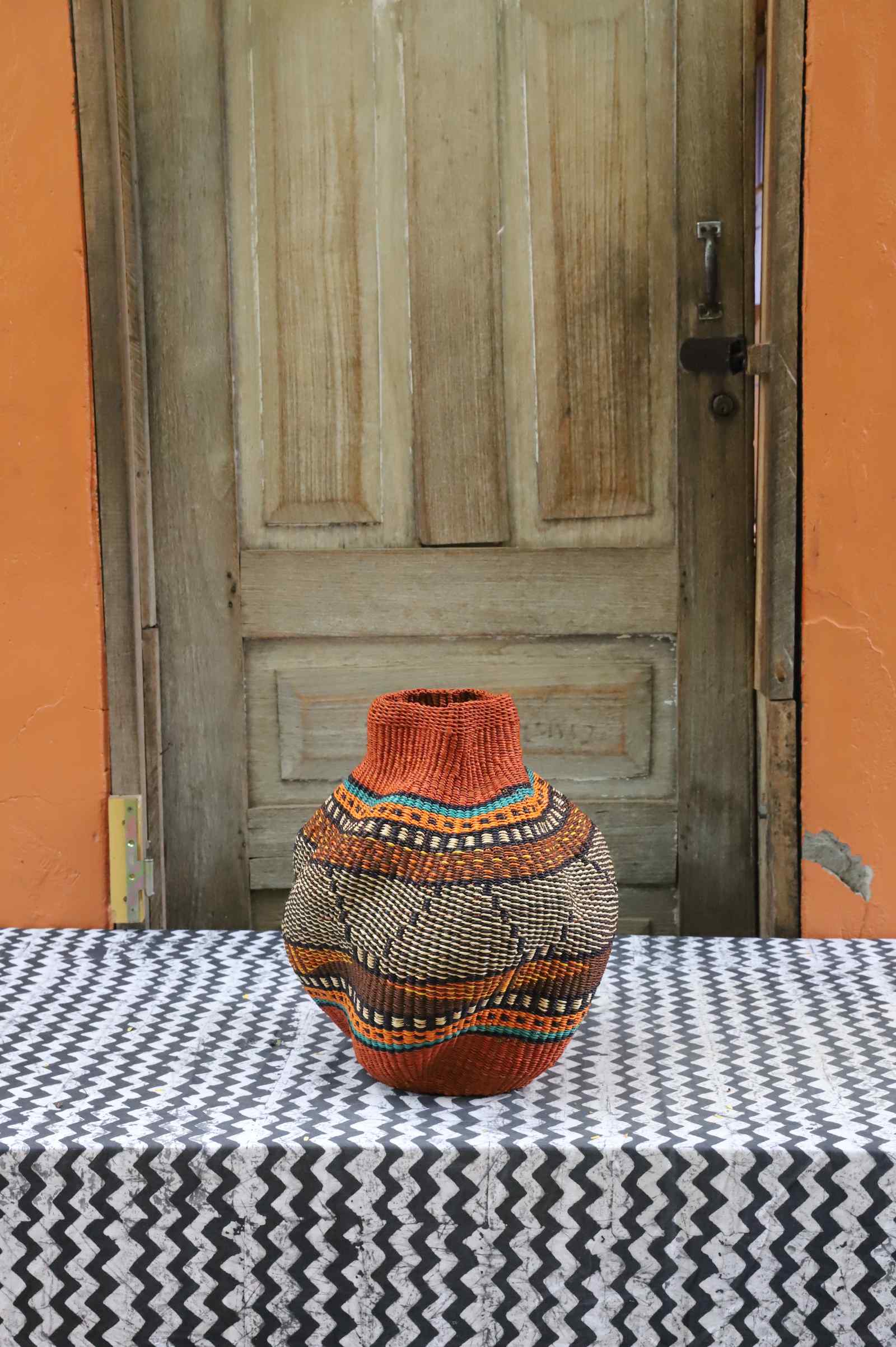 Handwoven Bolga art basket in a rounded pot shape with orange rim and natural body with dark diamond weave.