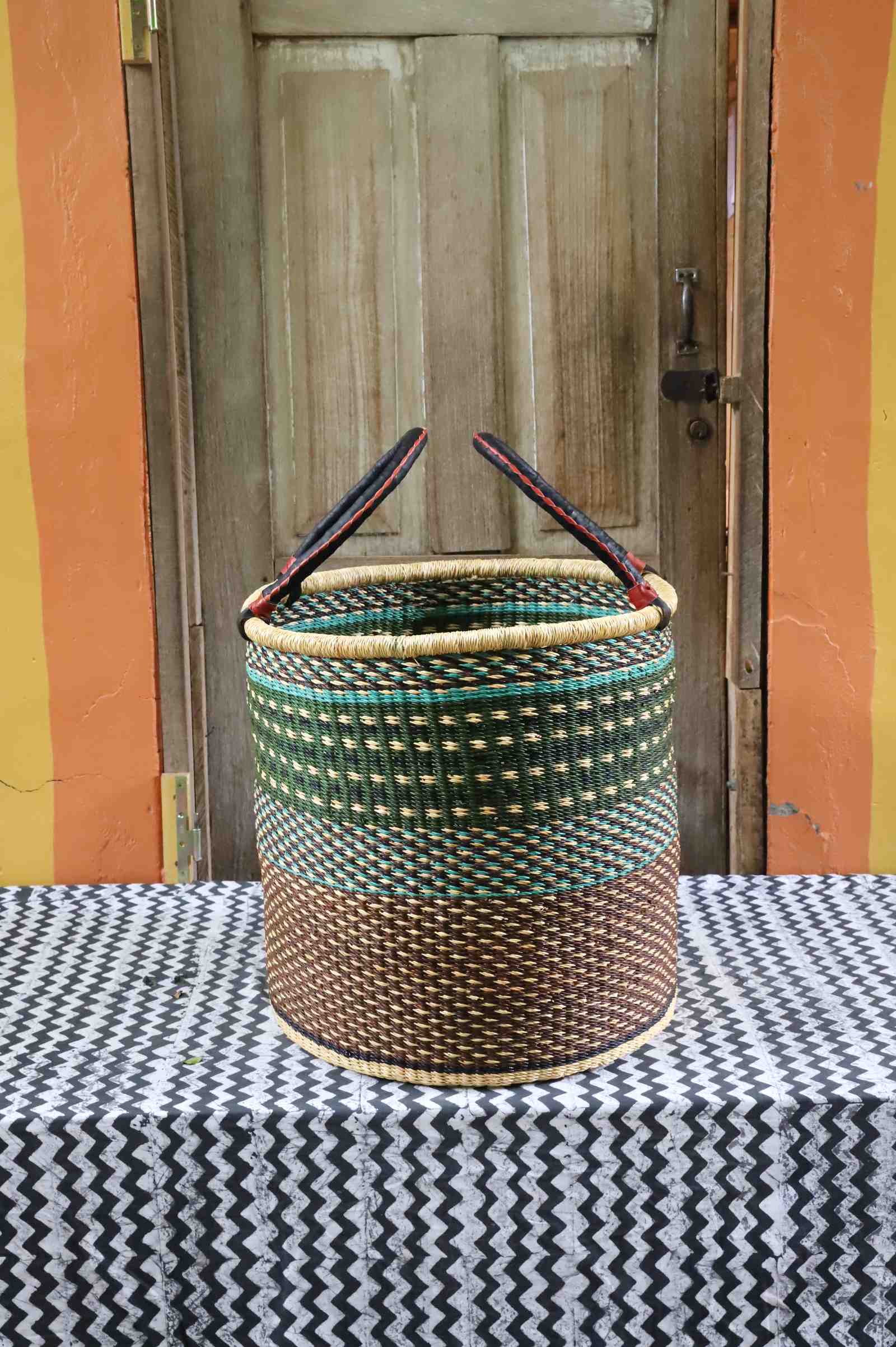 Large open laundry basket in green checkered weave with a dark brown base, styled on a chevron cloth.