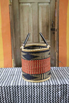 Open laundry basket in natural straw with an orange and black zigzag band, styled on a chevron cloth by a wooden door.