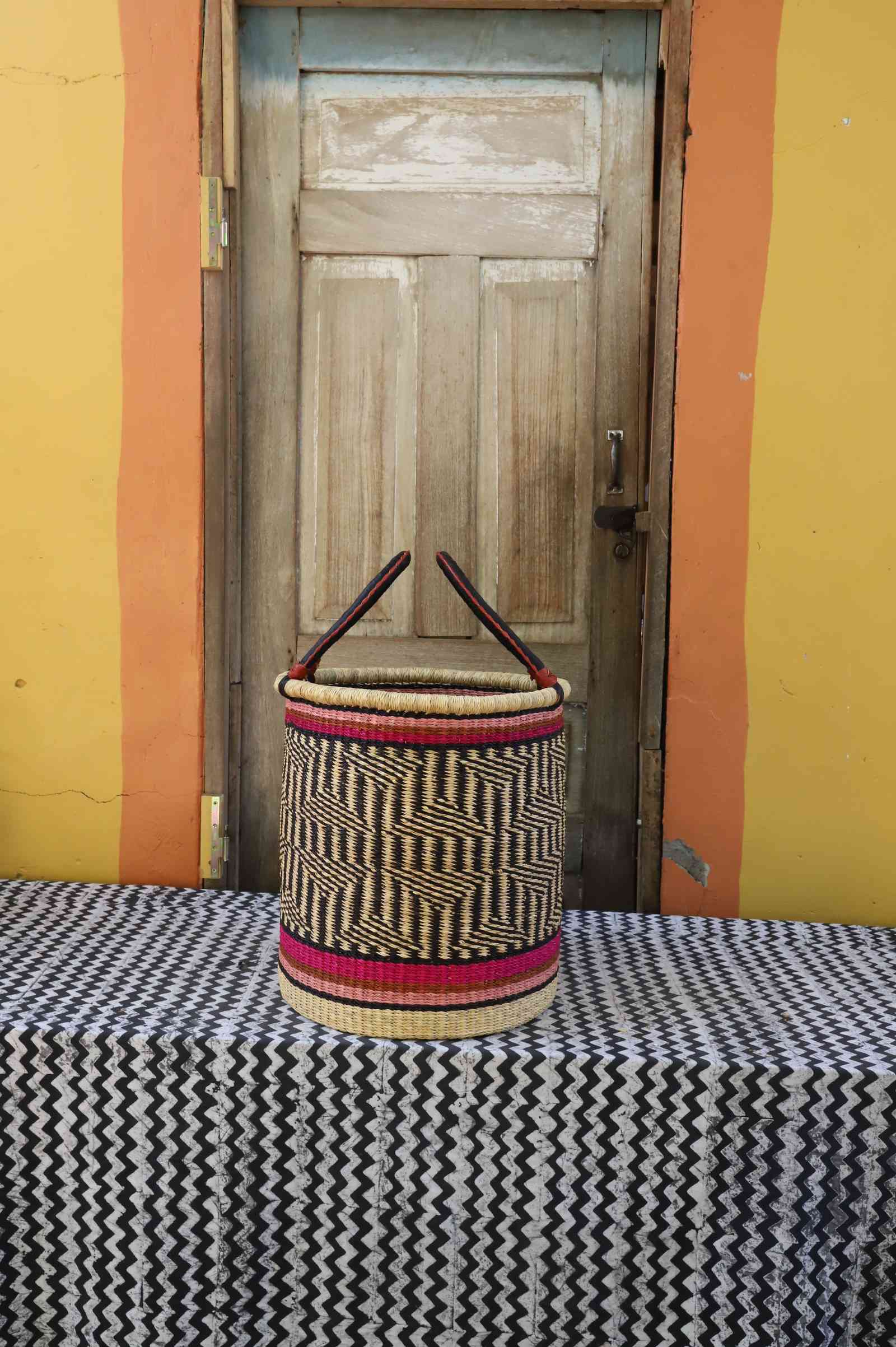 Small handwoven open-top Bolga laundry basket in natural straw with red bands and fine dark weave.
