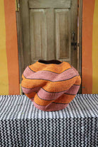 Large nest-shaped Bolga art basket in pink and rust wavy braided weave, styled on a chevron cloth by a wooden door.