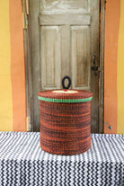 Handwoven Bolga laundry basket with lid in rust-orange elephant grass with a green banded rim.