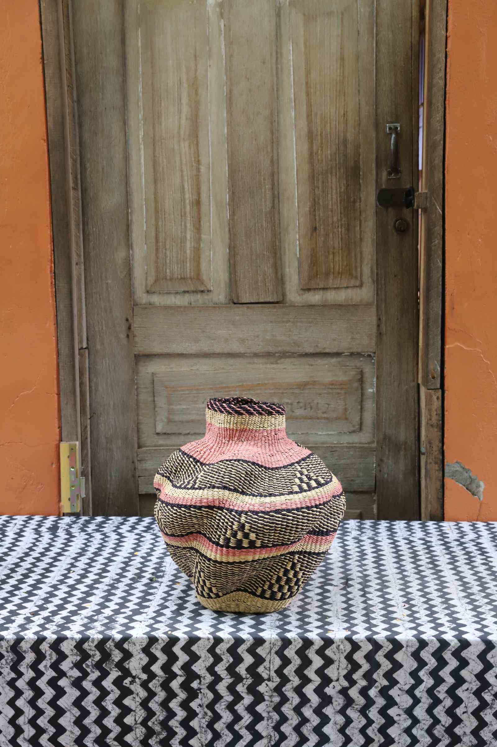 Handwoven Bolga art basket in a rounded pot shape, natural straw with pink and dark banded stripes.