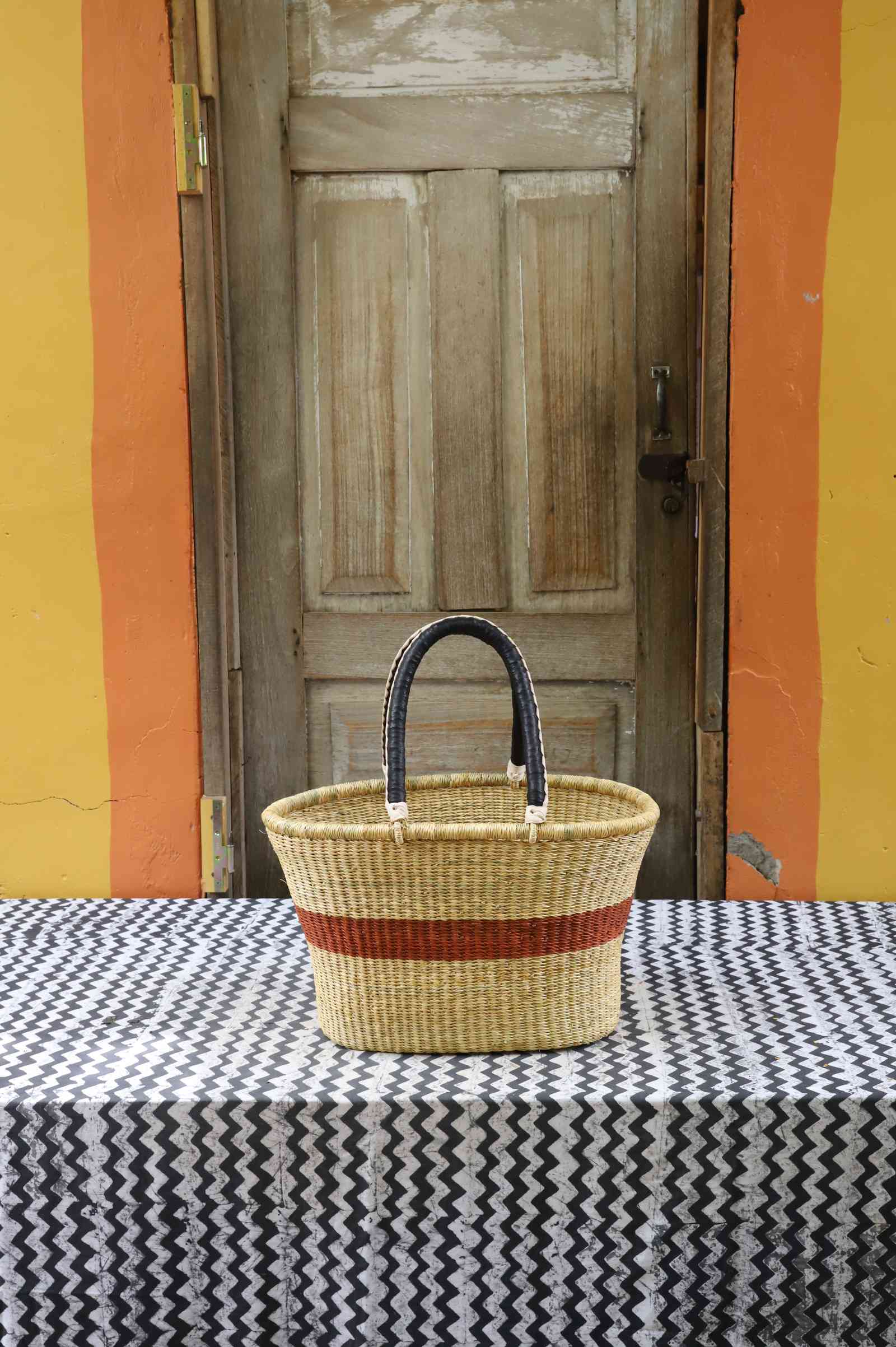 Large handwoven Bolga Zaane Tia market basket in natural straw with a rust-orange band and twin leather handles.