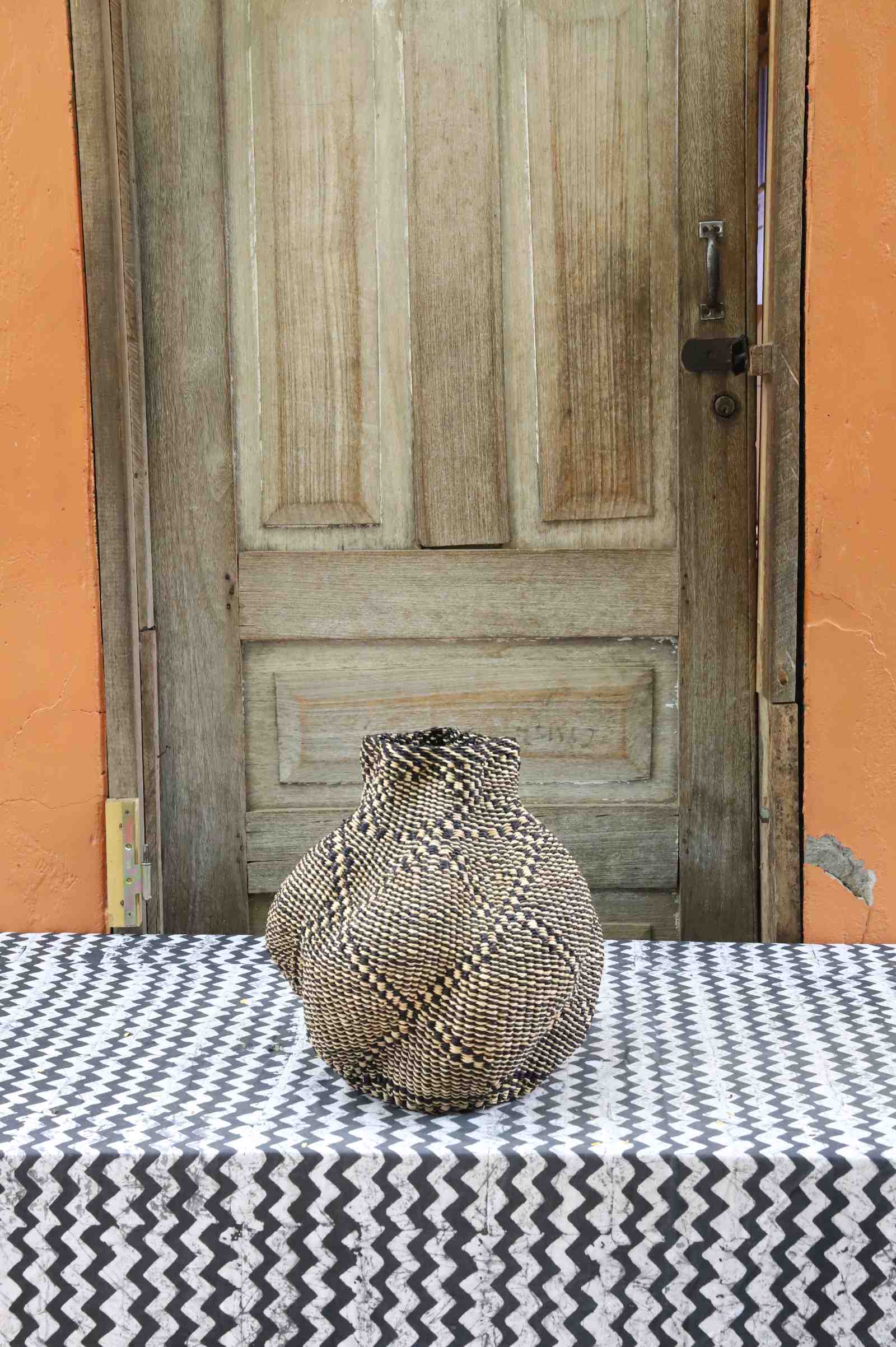Handwoven Bolga art basket in a rounded pot shape, natural straw with a fine dark diamond weave pattern.
