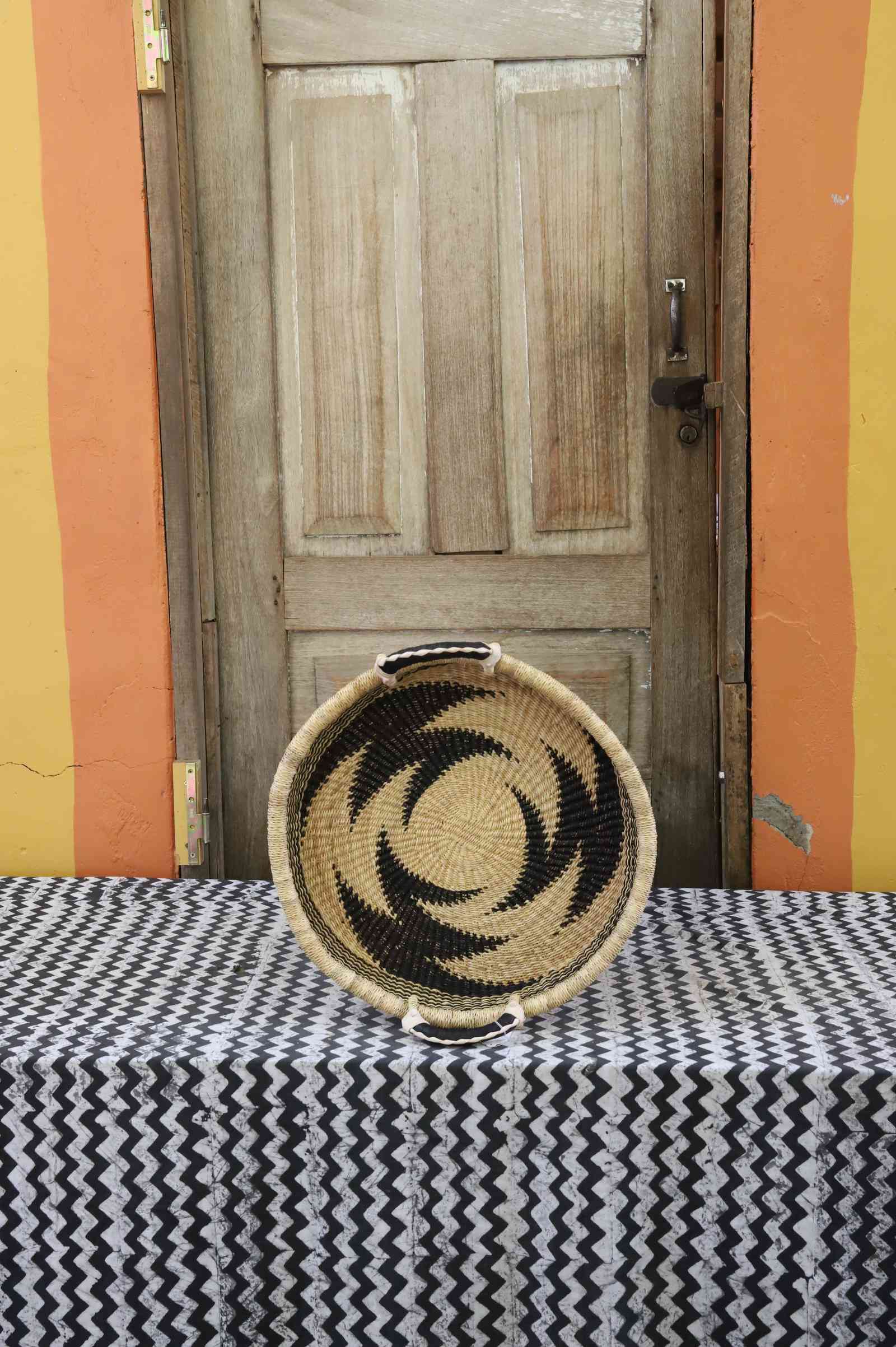 Handwoven Bolga wall tray disc in natural straw with a bold black star pinwheel pattern.