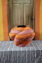 Large nest-shaped Bolga art basket in pink and rust wavy braided weave, front view on a chevron cloth.