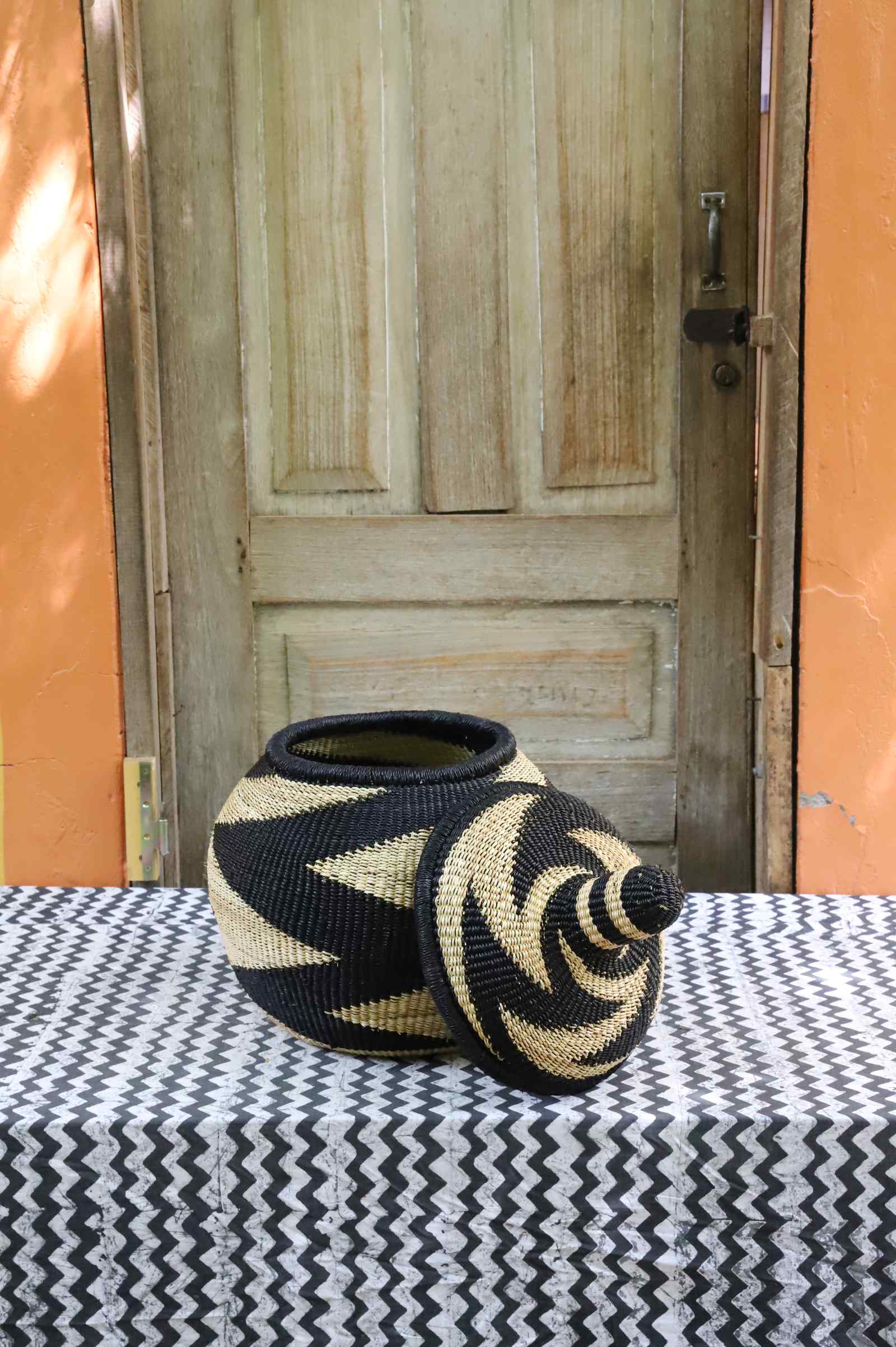 Lidded Bolga storage basket in a black and natural zigzag pattern, shown with its domed lid removed beside it.