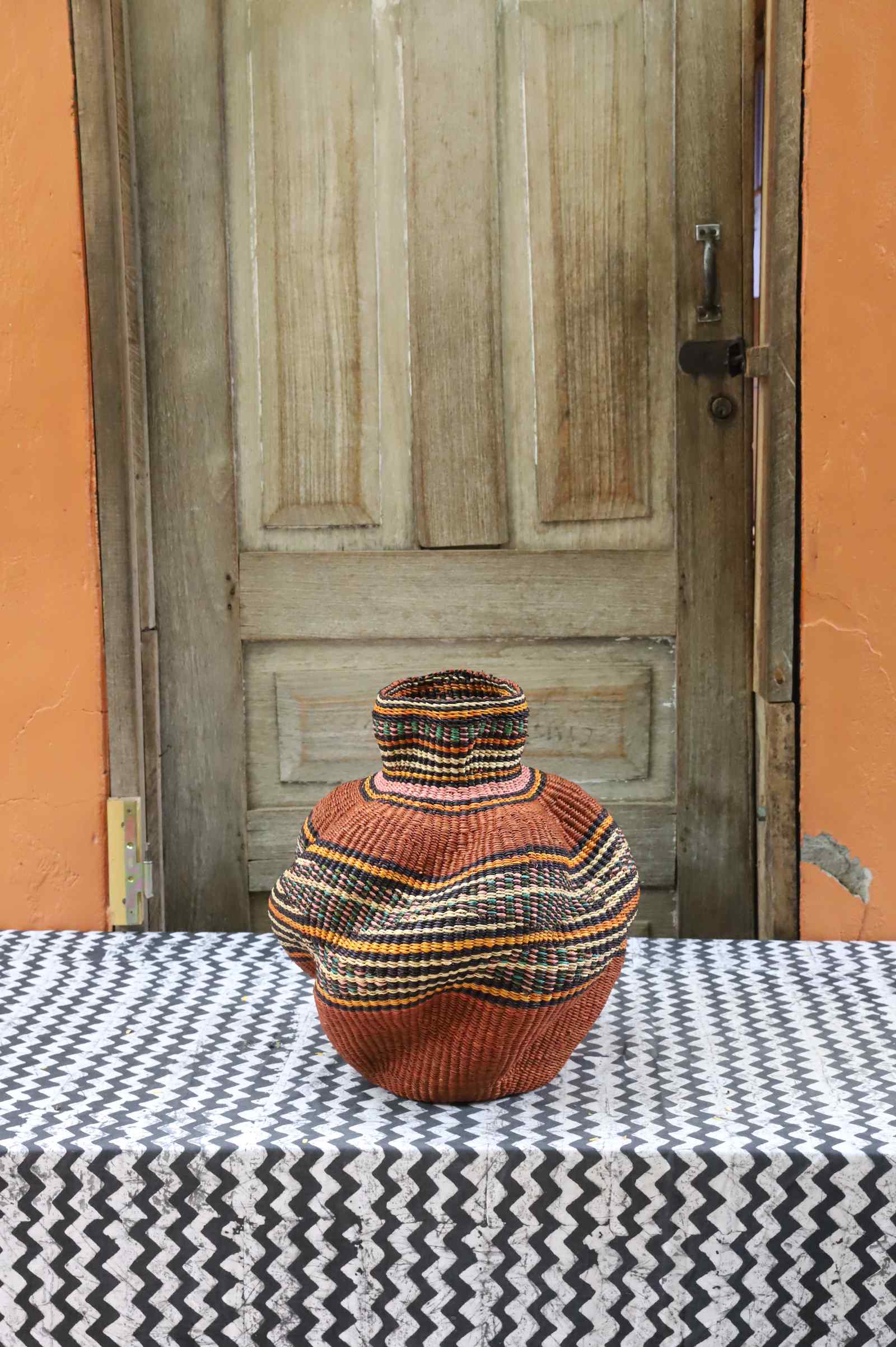 Handwoven Bolga art basket in a rounded pot shape, dyed rust-orange with a fine multicolour central band.