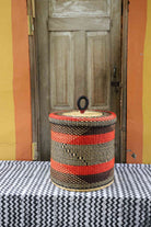 Handwoven Bolga laundry basket with lid in natural straw with red-orange stripes and a black diamond weave band.