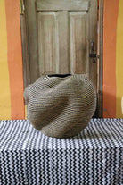 Large nest-shaped Bolga art basket in natural straw with a densely ridged weave, front view on a chevron cloth.