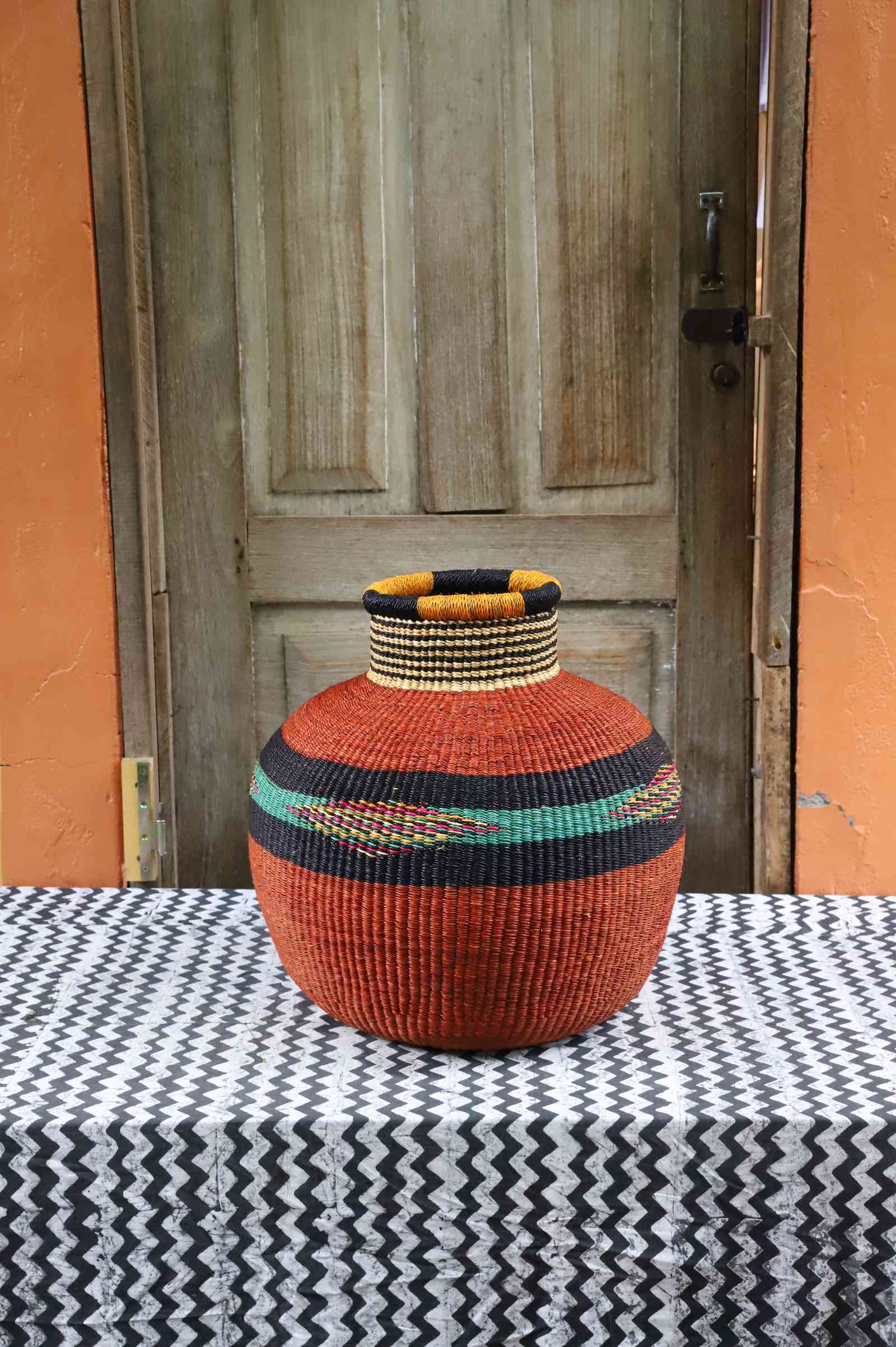 Round Bolga basket in terracotta with a black and cream striped neck and a green diamond-patterned band.