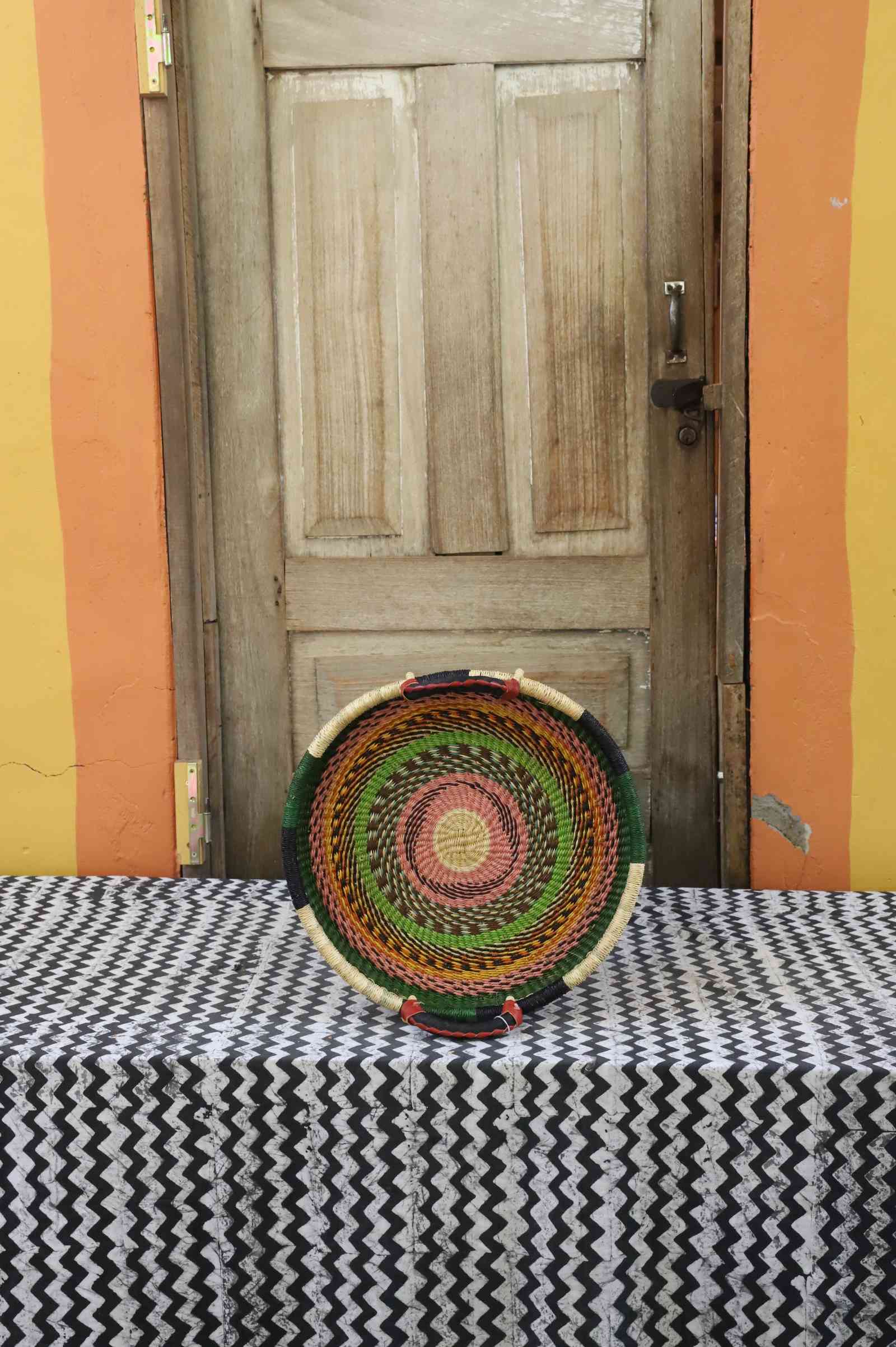 Handwoven Bolga wall tray disc in natural straw with red, green and orange banded rings.