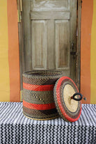Handwoven Bolga laundry basket with lid removed, showing red and black banded body and matching woven lid.