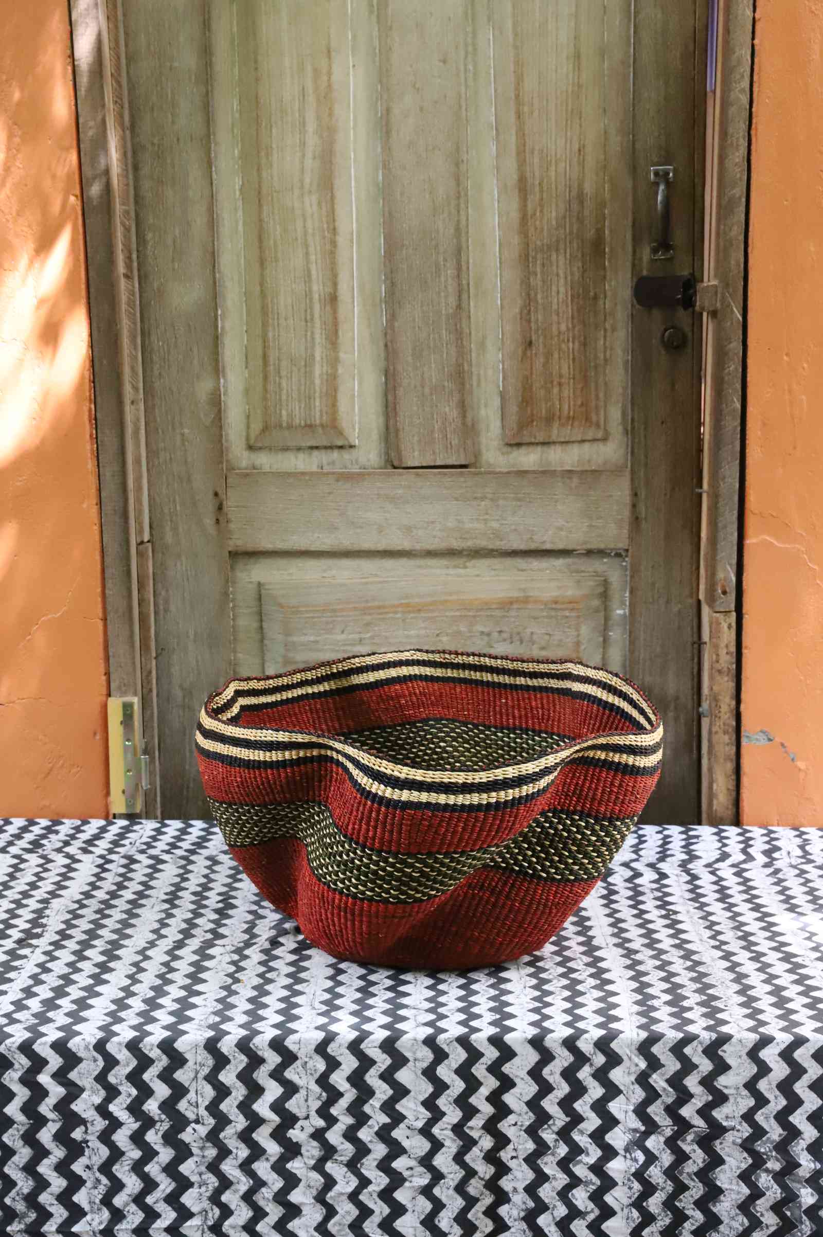 Wide wave-rimmed Bolga basket in rust red with a black and gold wave-patterned band, styled on a tablecloth.