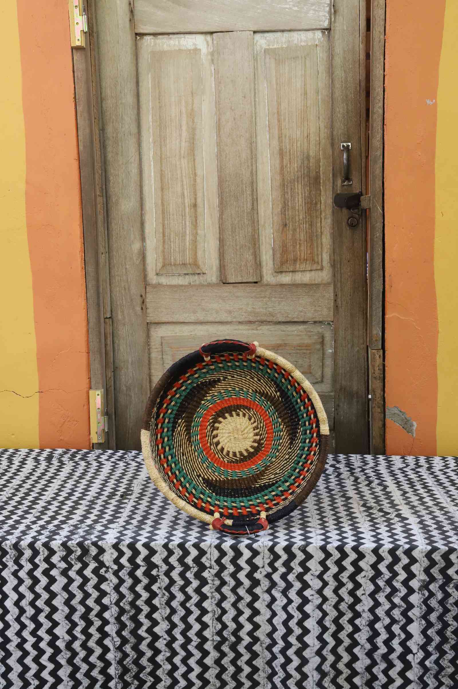 Handwoven Bolga wall tray disc with dark rim, green and orange concentric bands and yellow centre.