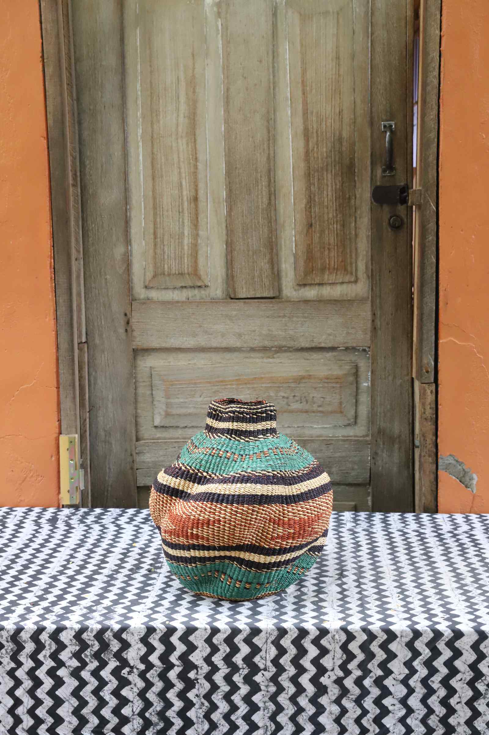 Handwoven Bolga art basket in a rounded pot shape, natural straw with dark bands and a red central section.