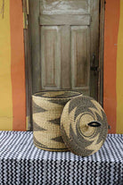 Handwoven Bolga laundry basket with lid shown removed, showing a natural-straw interior and zigzag exterior.