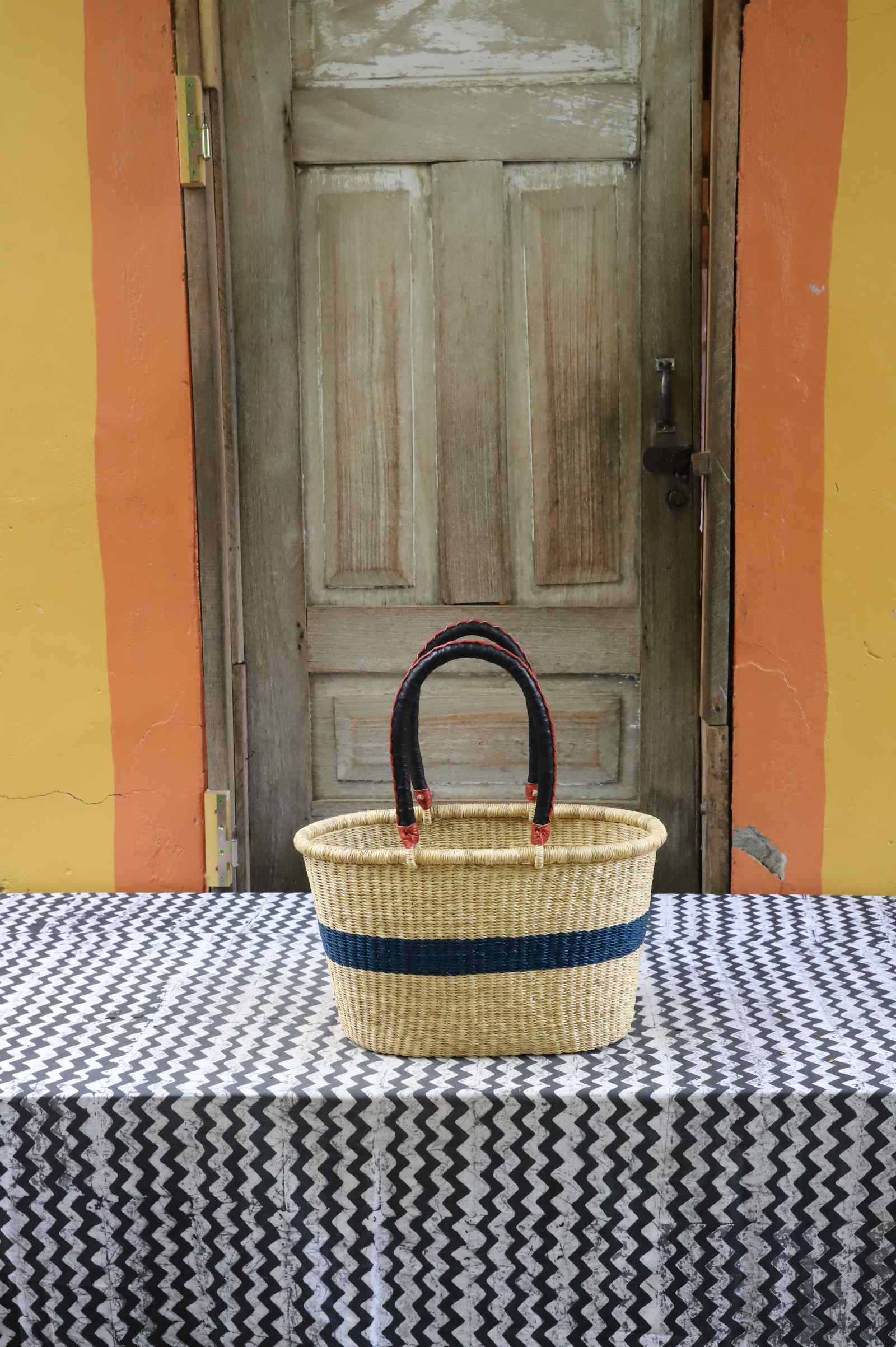 Medium handwoven Bolga Zaane Tia market basket in natural straw with a navy band and twin leather handles.